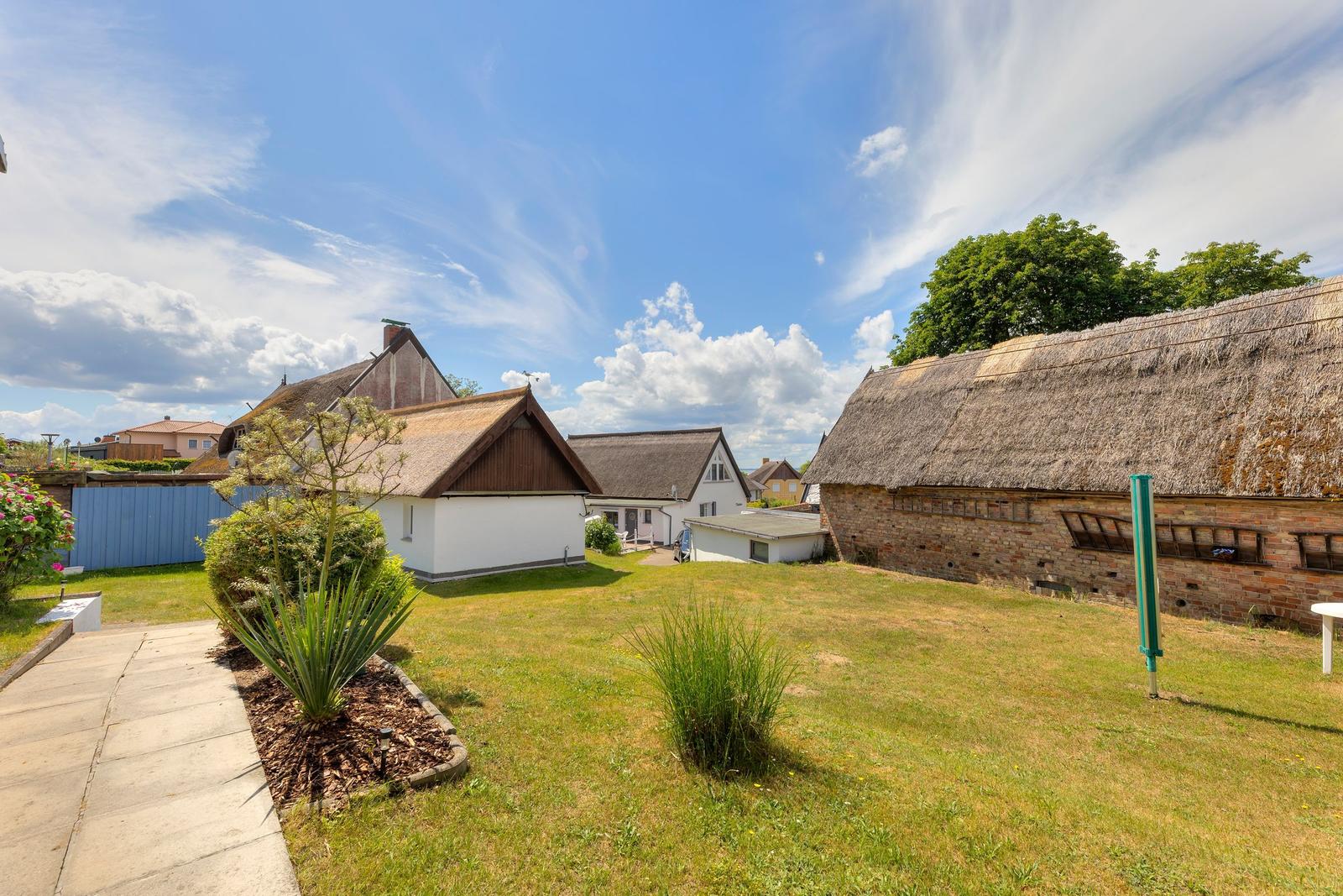 Grüner Garten mit traditionellen Häusern und strohgedeckten Dächern unter blauem Himmel.