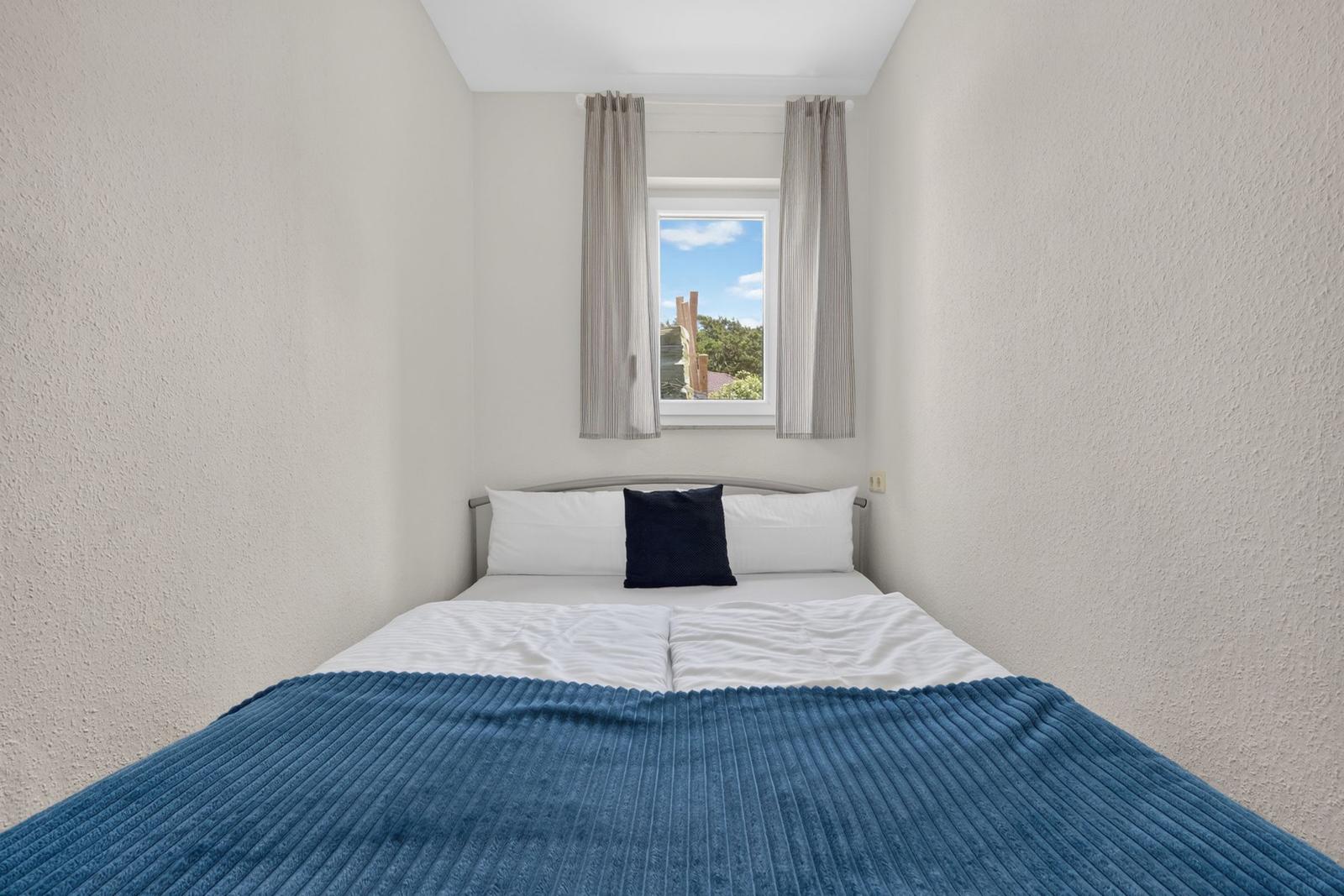 Ein Schlafzimmer mit einem Bett, blauer Decke und Fenster mit Blick auf Grün.