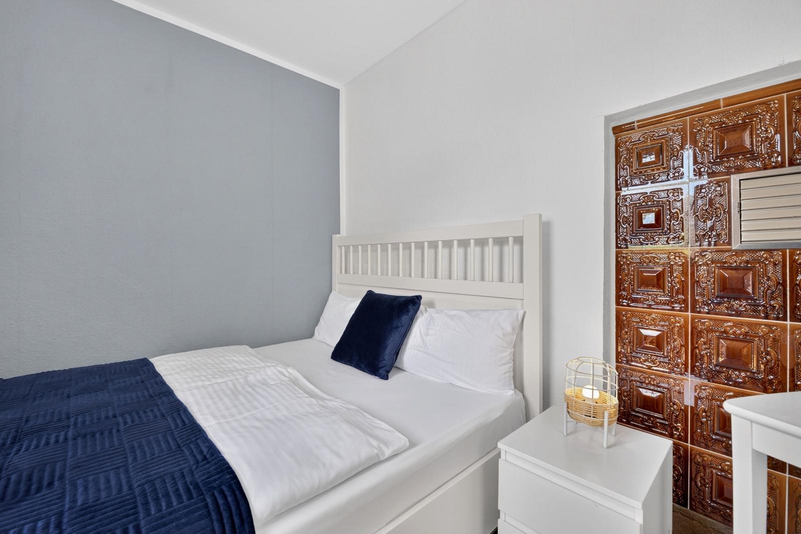 Schlafzimmer mit weißem Bett, blauer Decke und Holzfliesenwand