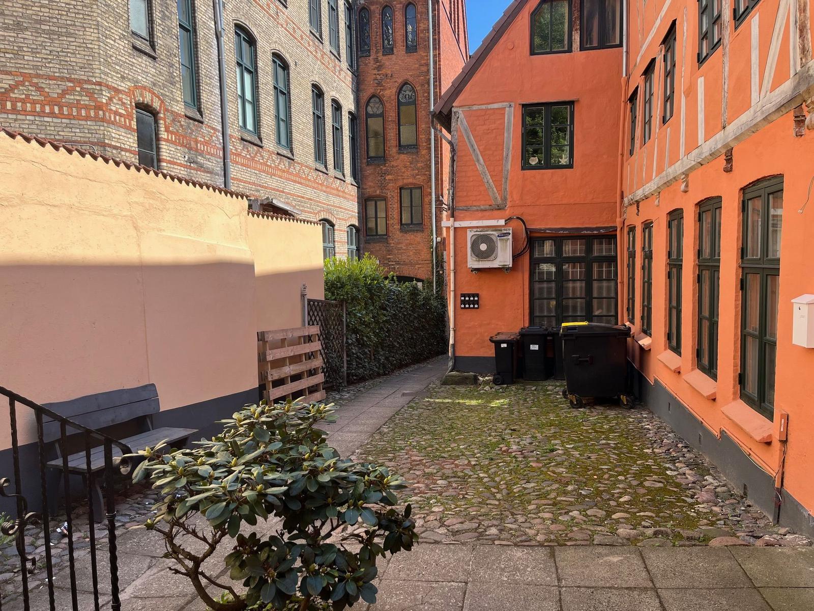 Hinterhof mit Steinweg, orangefarbener Fachwerkhauswand und Sitzbank.