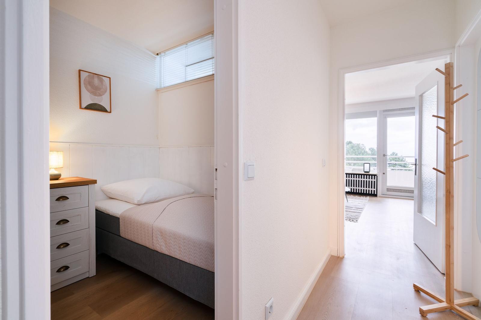 Bedroom with bed, nightstand, and picture. Passage to living area with balcony.