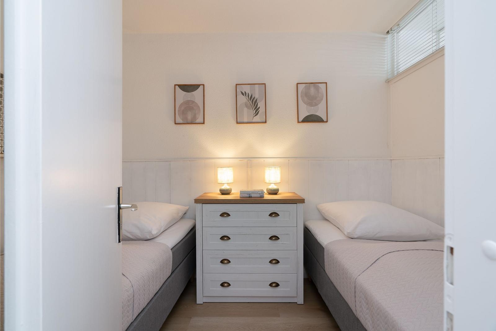 Two single beds flank a dresser with two lamps and three pictures on the wall.