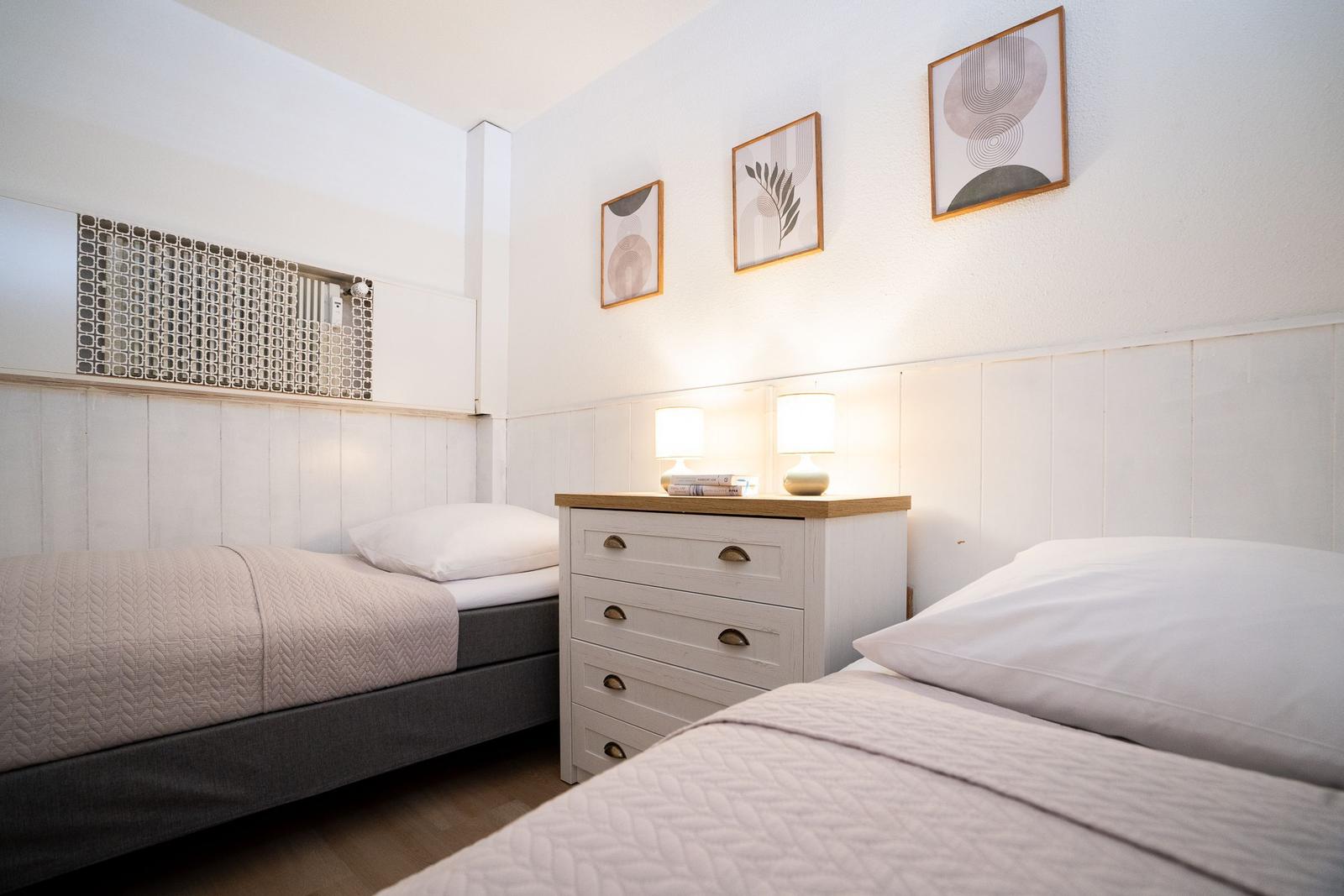 Two beds with white pillows and light bedspreads. Between them stands a dresser with two lamps.