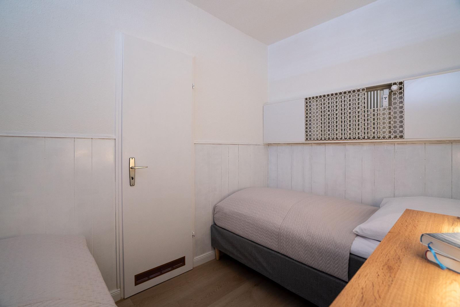 Bedroom with bed, desk, and door. Wall paneling and decorative element.