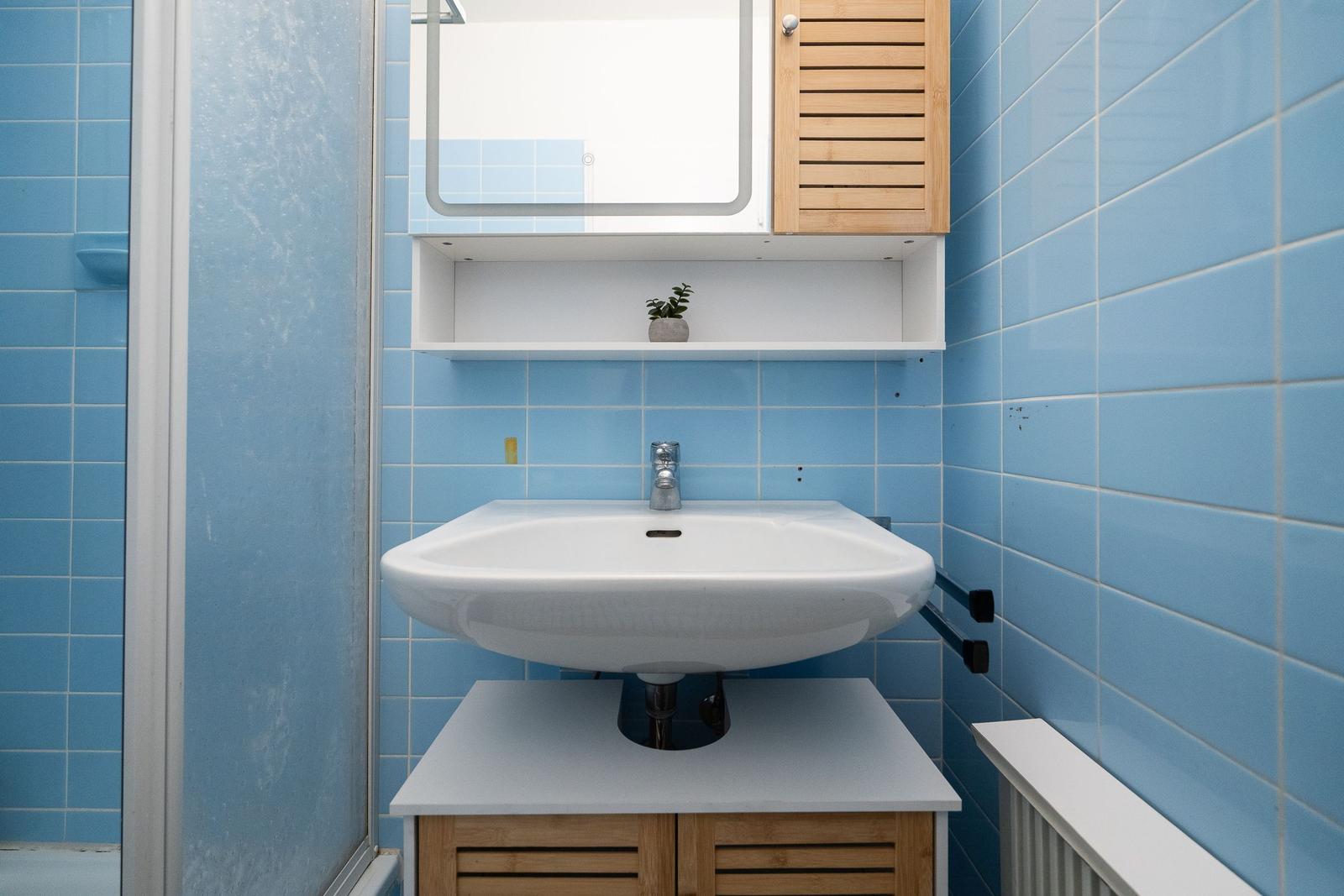 Bathroom with blue tiles, sink, and mirror cabinet.
