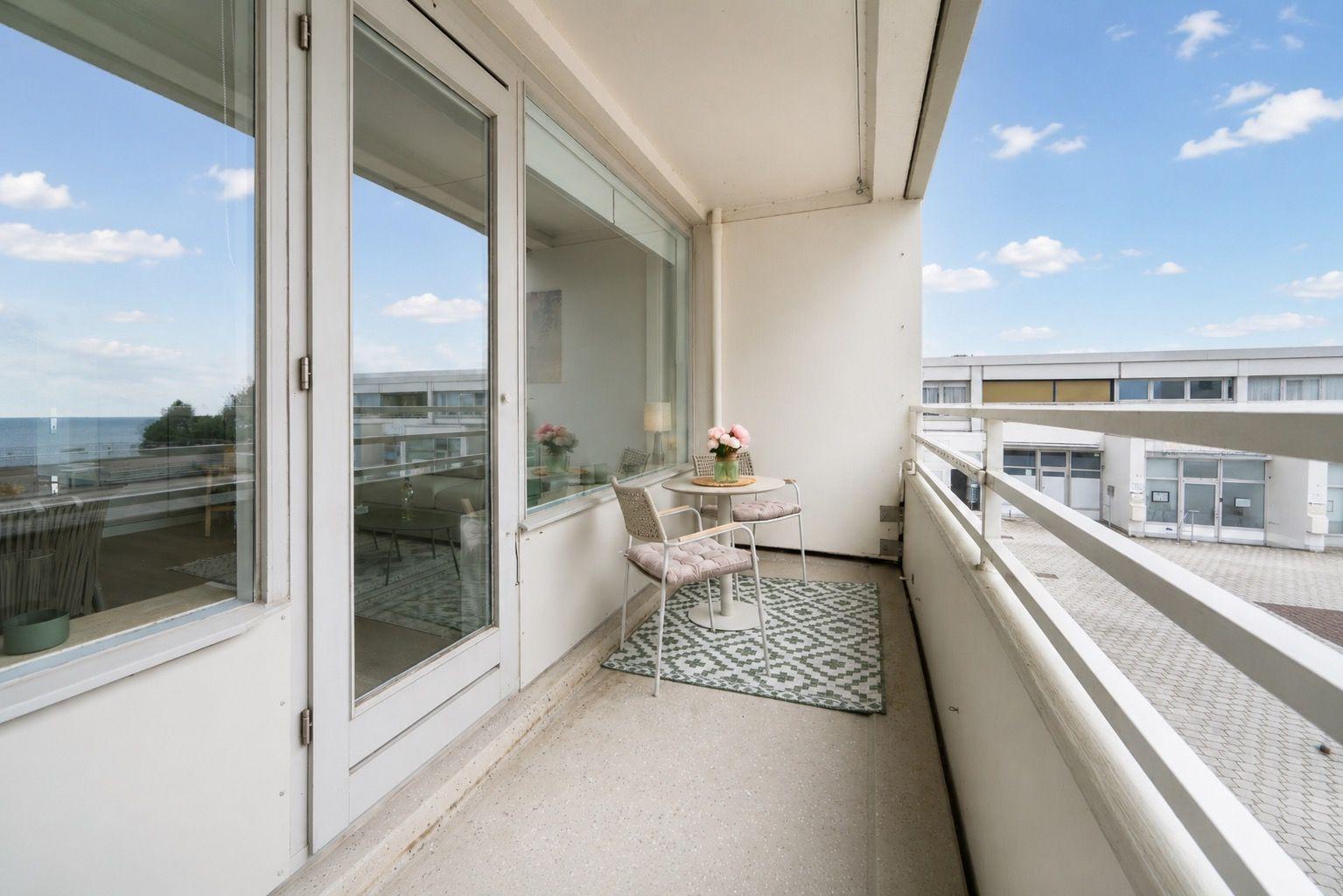 Balcony with table, chairs, and flowers. View of the sea and buildings.