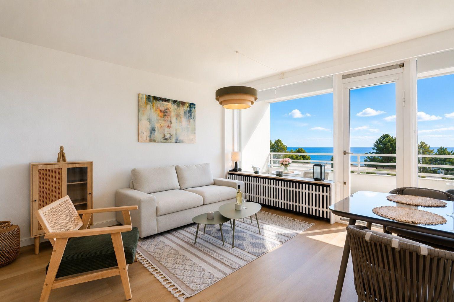 Living area with sofa, dining table, and balcony with sea view.