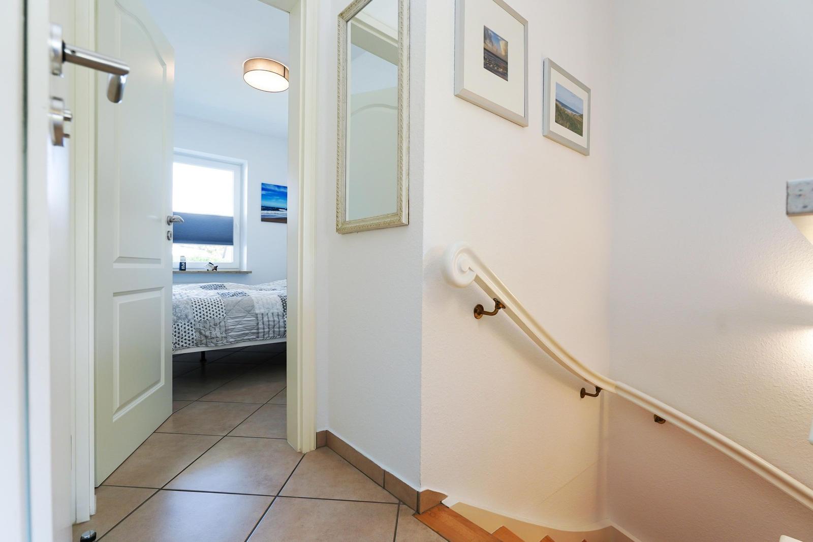 Hausflur mit Treppe und Blick in Schlafzimmer mit Bett und Fenster.