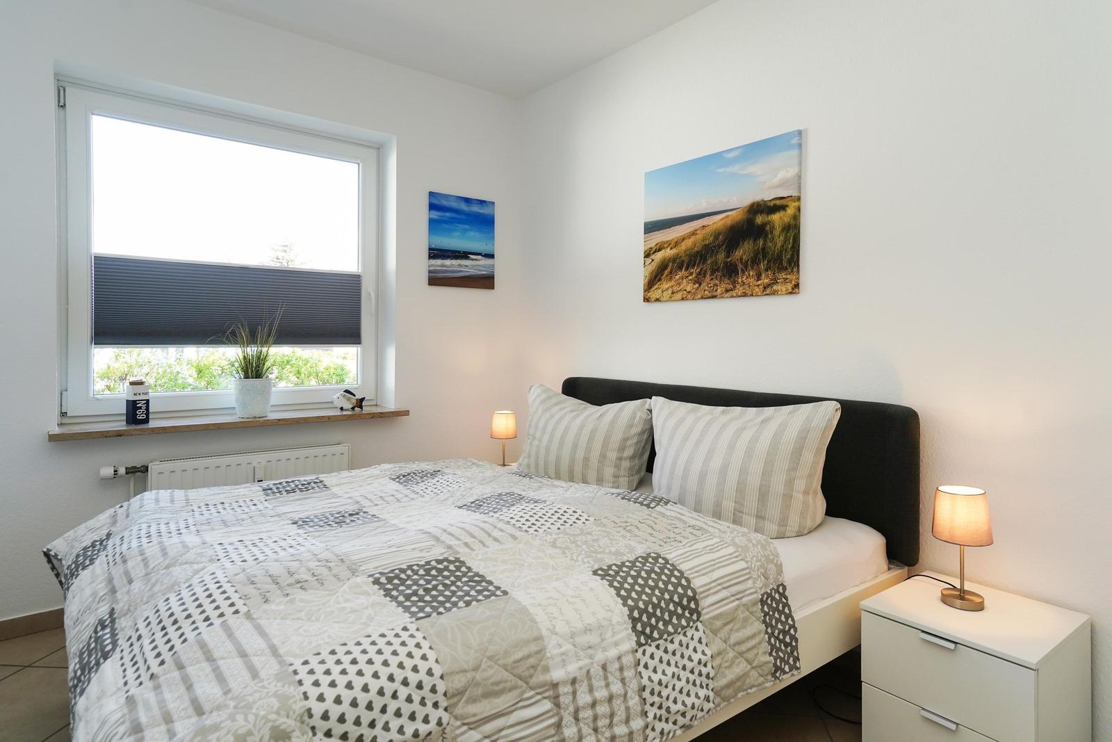 Schlafzimmer mit Bett, Nachttisch und Fenster. An den Wänden hängen Bilder.