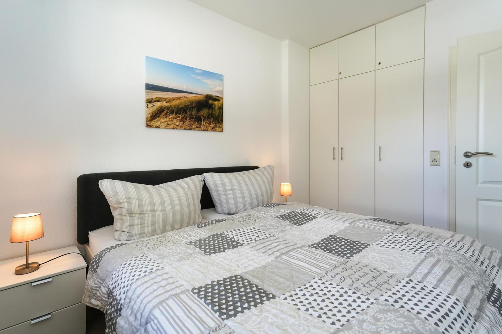 Schlafzimmer mit Bett, Nachttisch, Kleiderschrank und Wandbild.