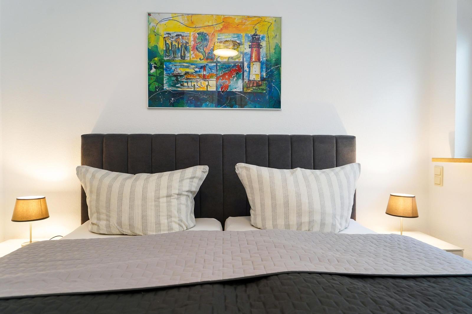 Doppelbett mit Kissen und Wandbild über dem Kopfteil.