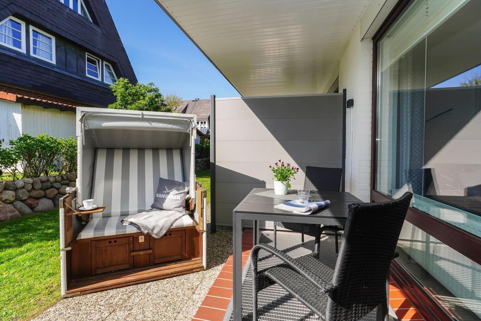 Terrasse mit Liegestuhl, Tisch und Stühlen. Hintergrund: Haus und Grünfläche.