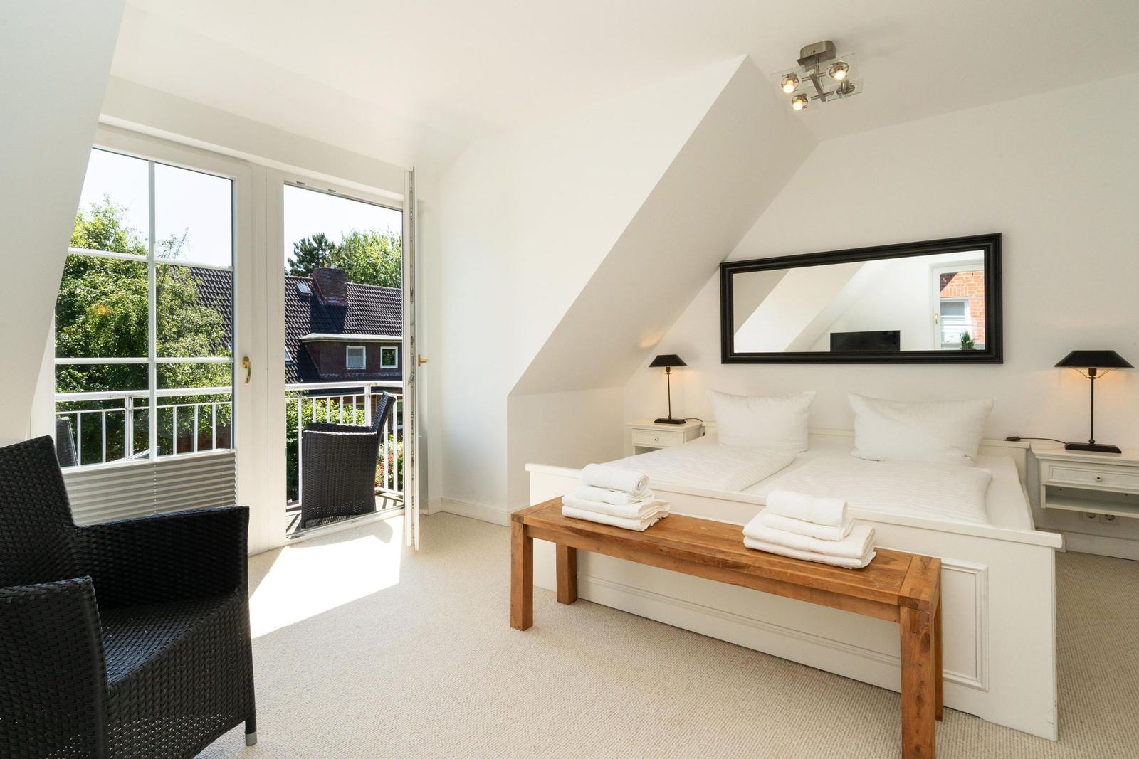 Schlafzimmer mit Dachschrägen, Balkon, Bett und Holzbank.