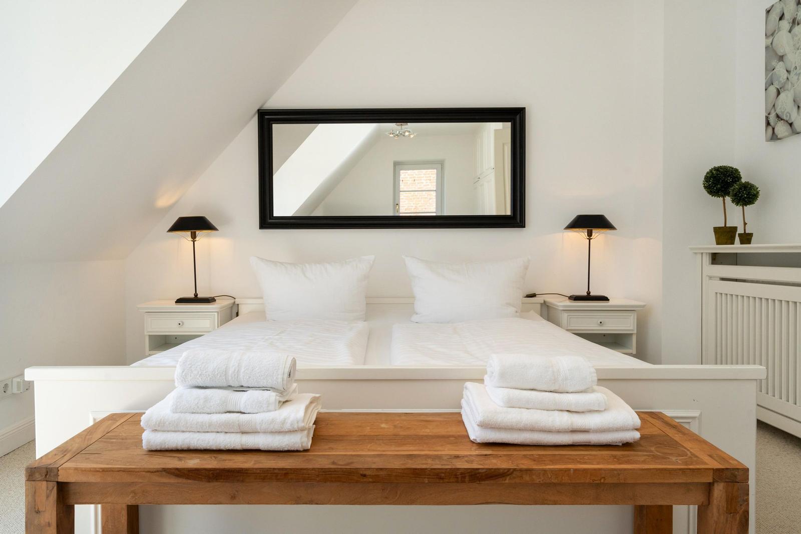 Schlafzimmer mit weißem Bett, zwei Nachttischen und Spiegel an der Wand.