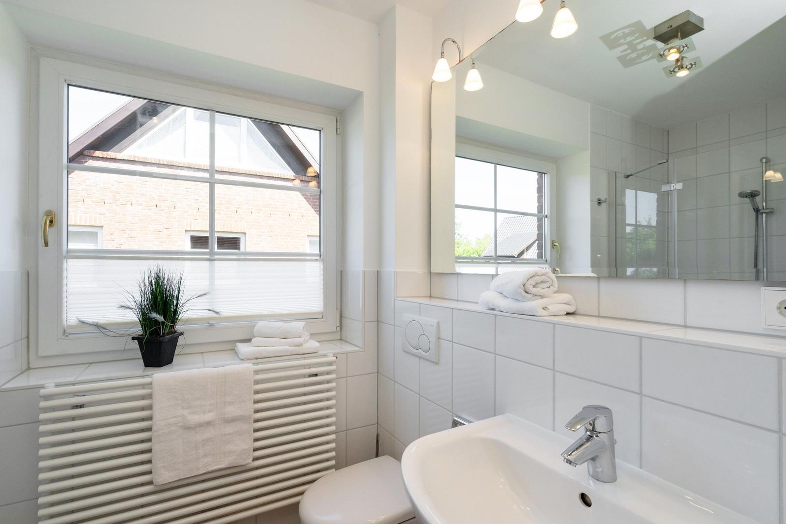 Badezimmer mit Fenster, Spiegel, Waschbecken und Dusche.
