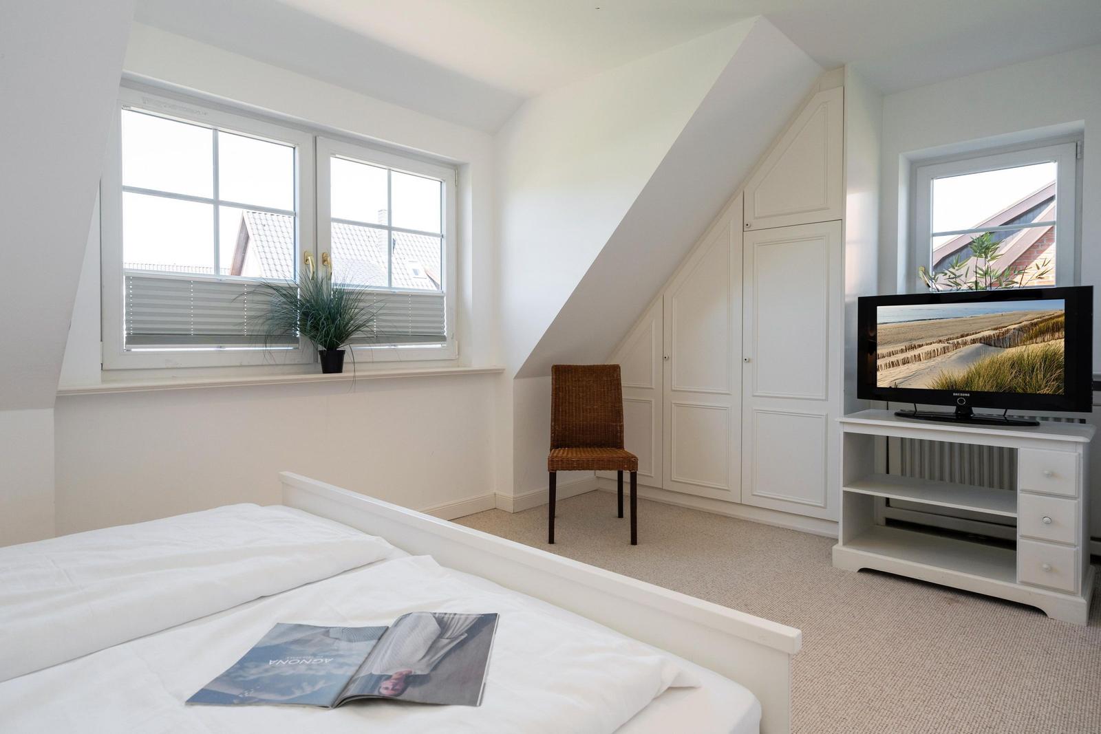 Schlafzimmer mit Dachschräge, Bett, TV und Kleiderschrank.