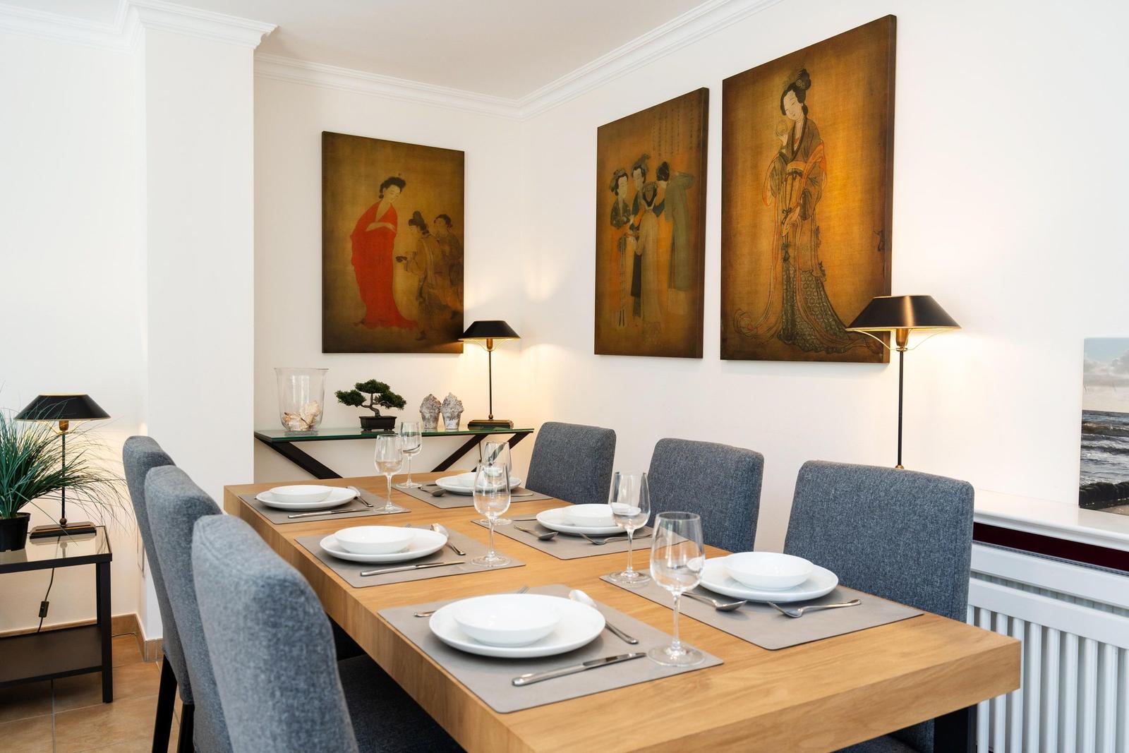 Esszimmer mit Holztisch, grauen Stühlen und drei Wandbildern mit asiatischen Motiven.