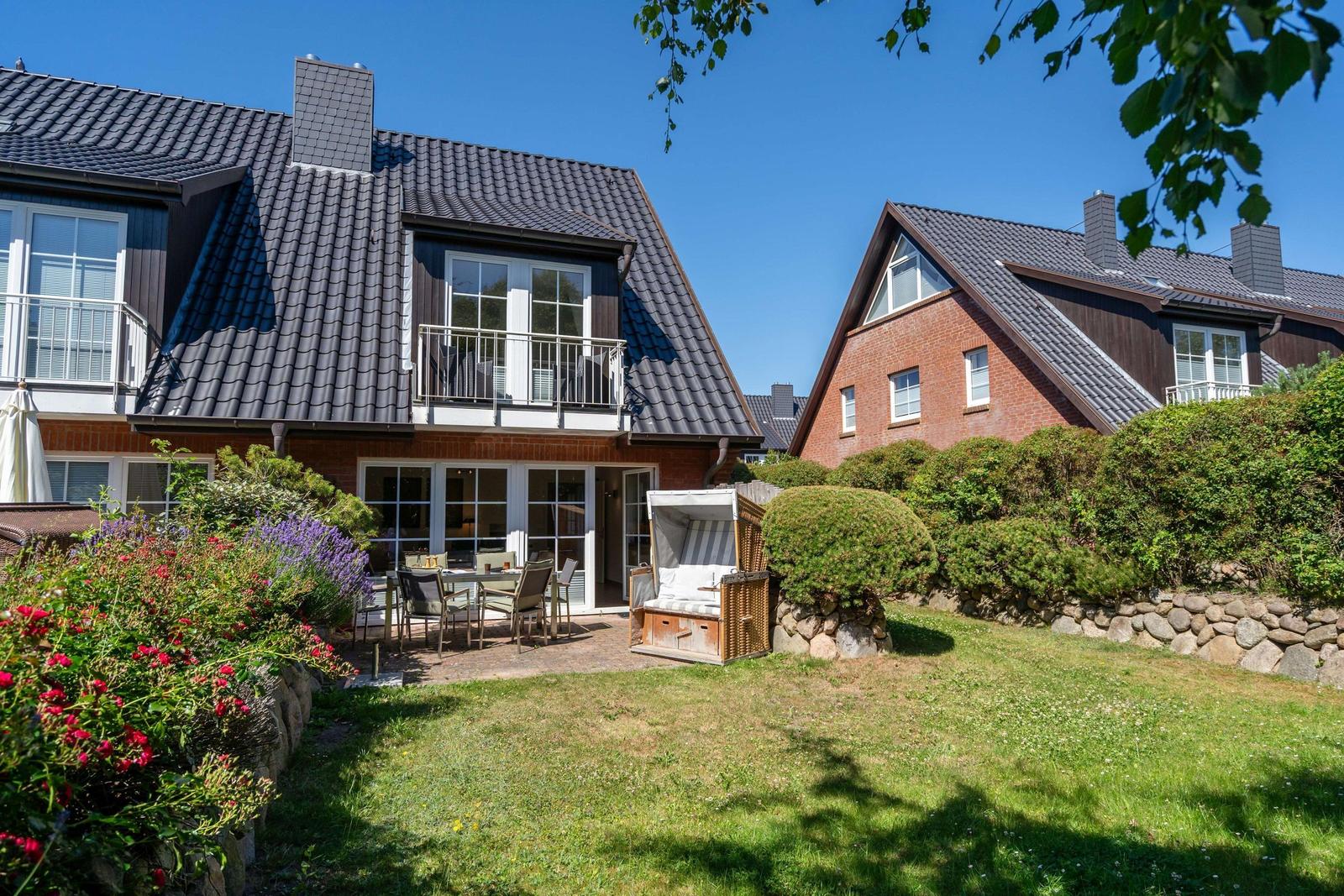 Haus mit Garten, Terrasse und Strandkorb. Blumen und Gras sind sichtbar.