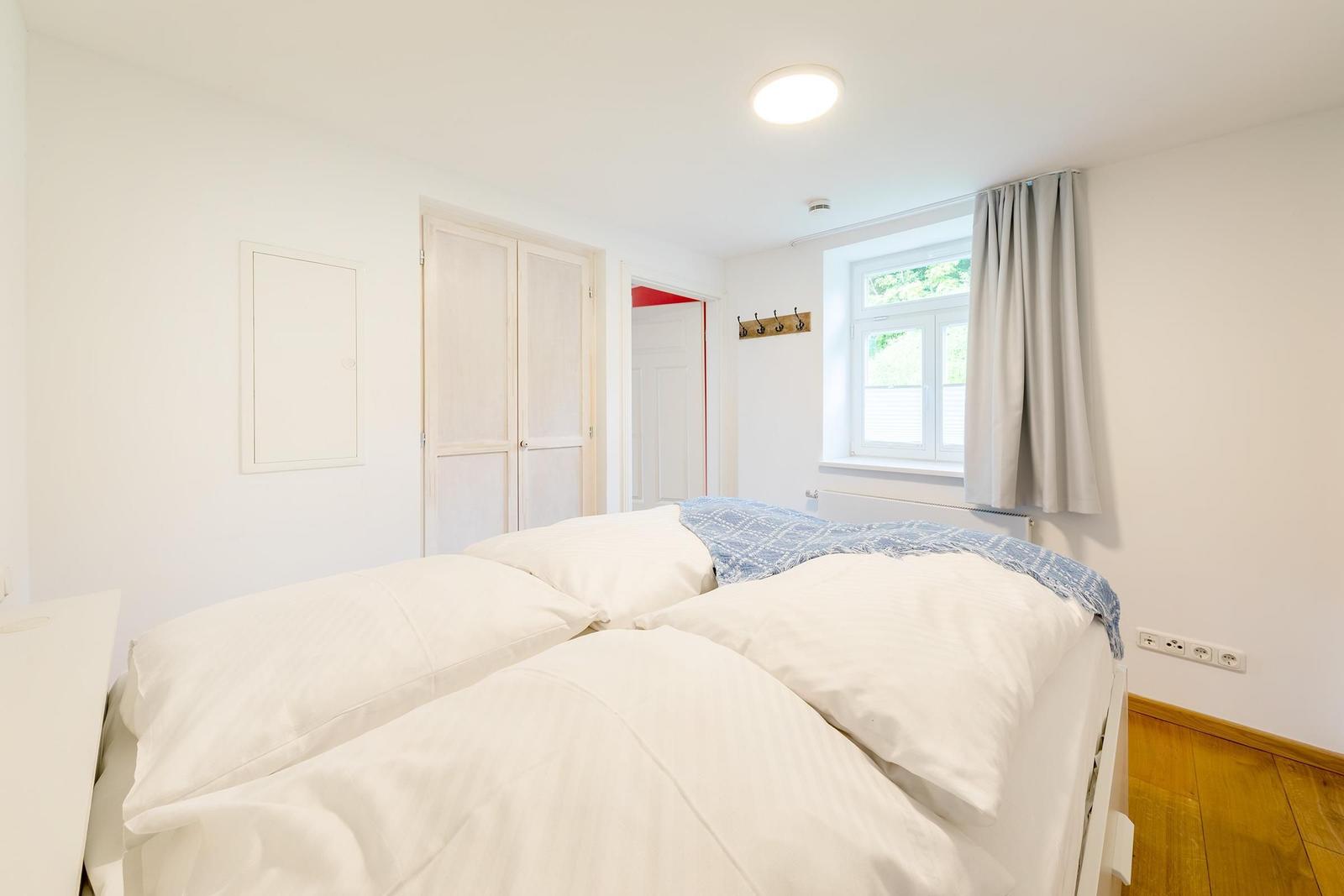 Schlafzimmer mit Bett, Fenster und Kleiderhaken an der Wand.