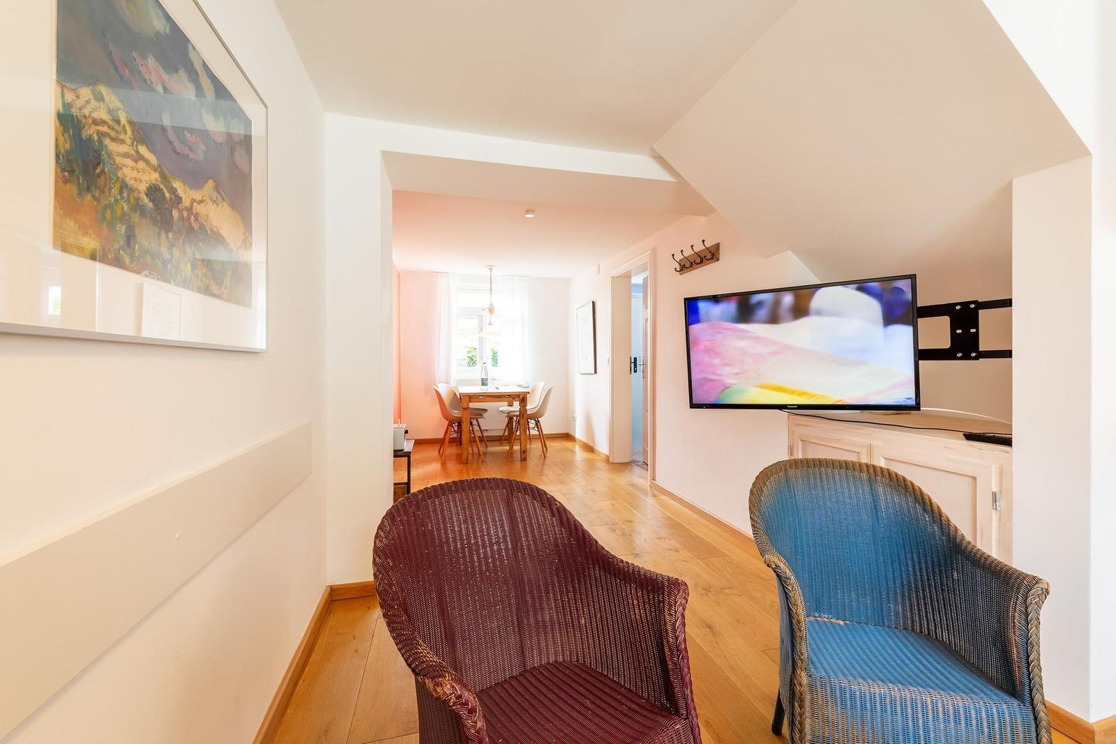 Zwei Stühle vor Fernseher, Essbereich im Hintergrund, Wandbild und Holzboden