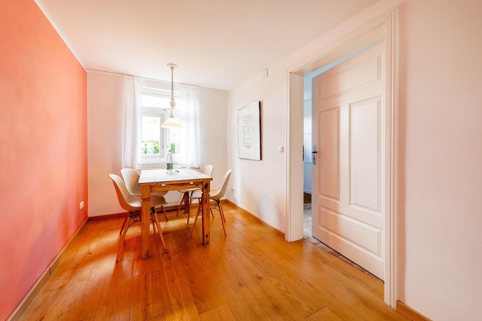Esszimmer mit Holztisch, vier Stühlen und Fenster. Tür führt in einen anderen Raum.