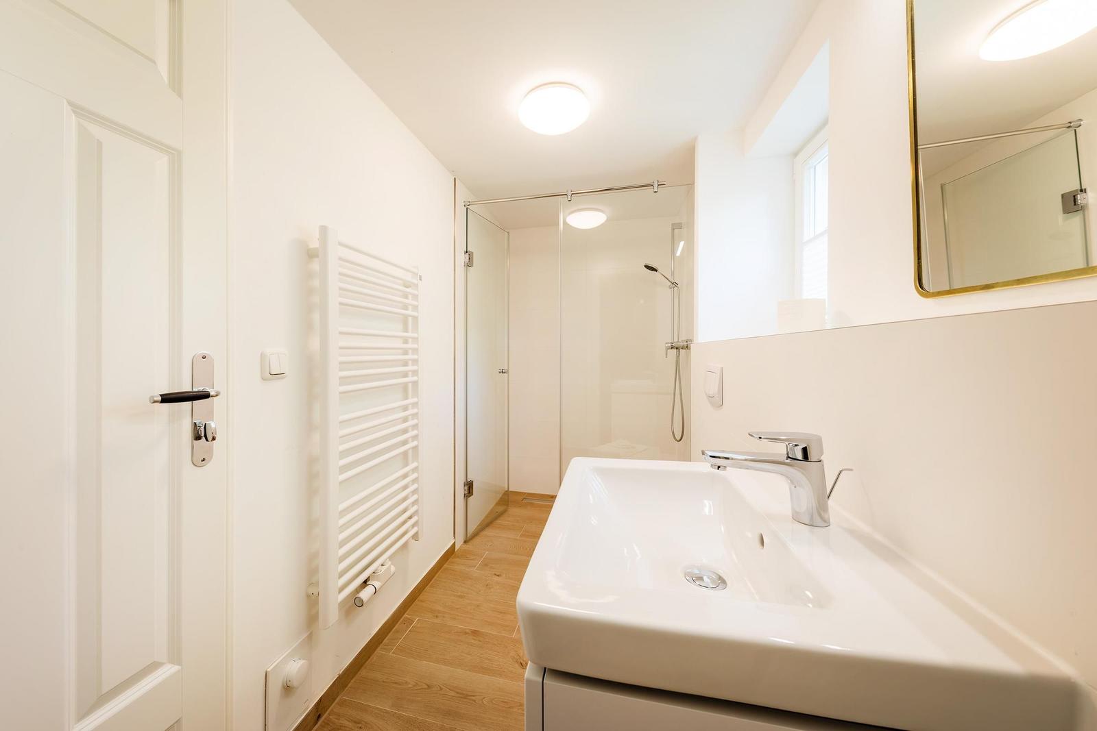 Badezimmer mit Dusche, Waschbecken und Heizung.