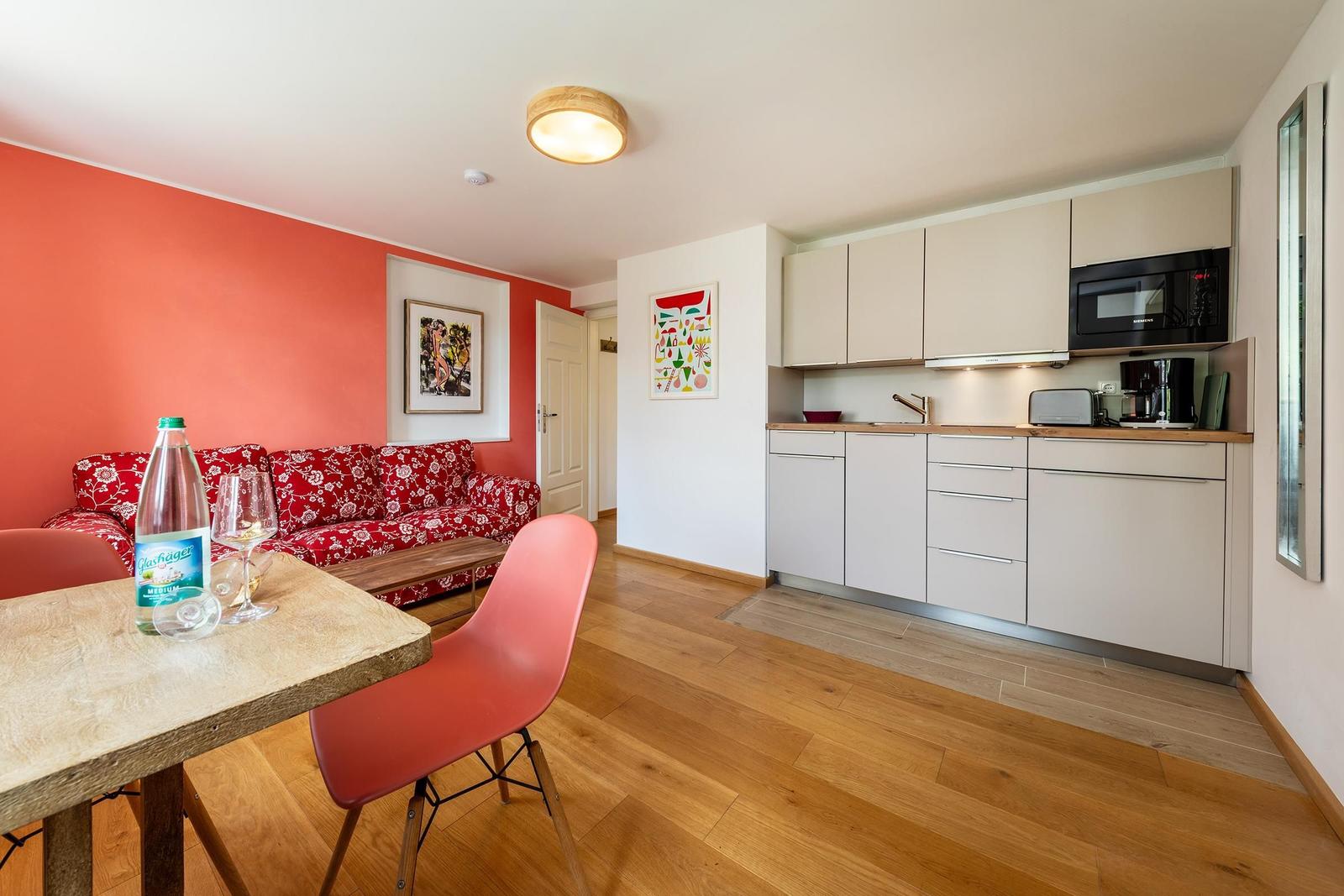 Wohnküche mit rotem Sofa, Holzboden und Küchenschränken.