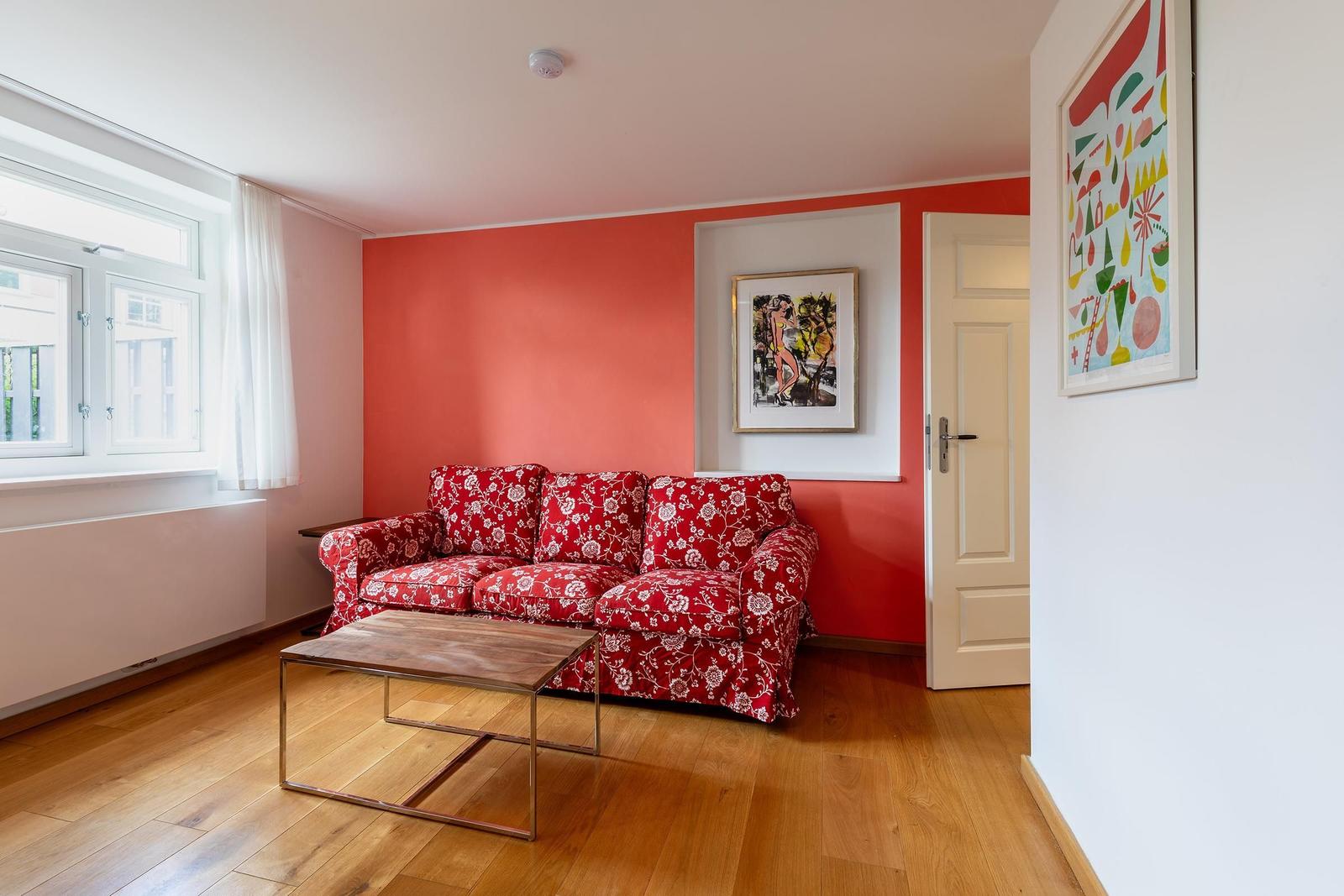Wohnzimmer mit rotem Sofa, Holzboden und Fenster. Wand mit Bildern.