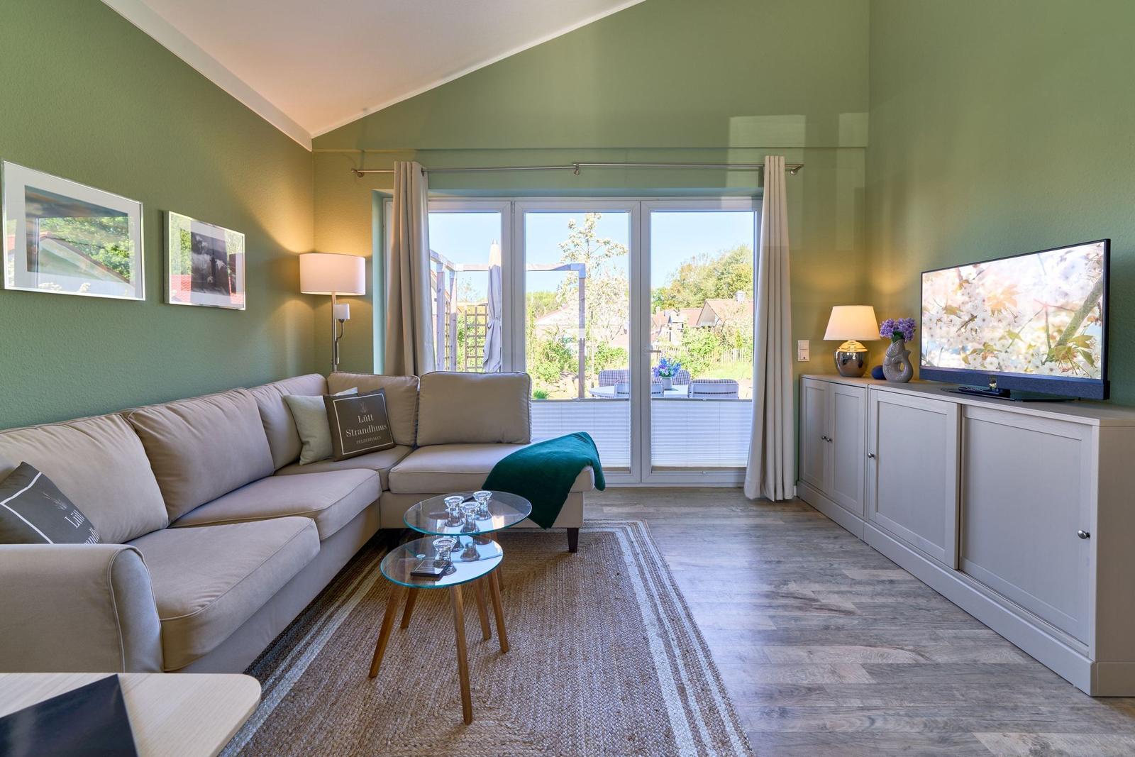 Wohnzimmer mit Sofa, TV und Blick auf Balkon.