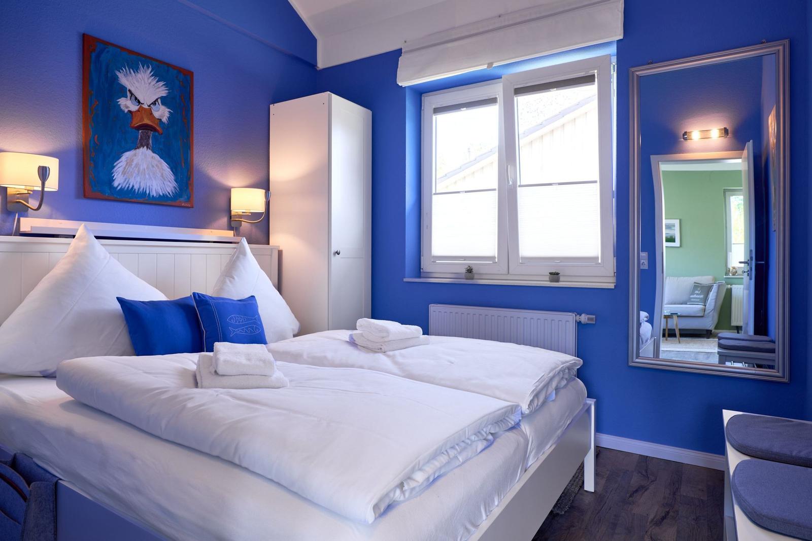 Schlafzimmer mit blauen Wänden, Bett, Spiegel und Fenster.