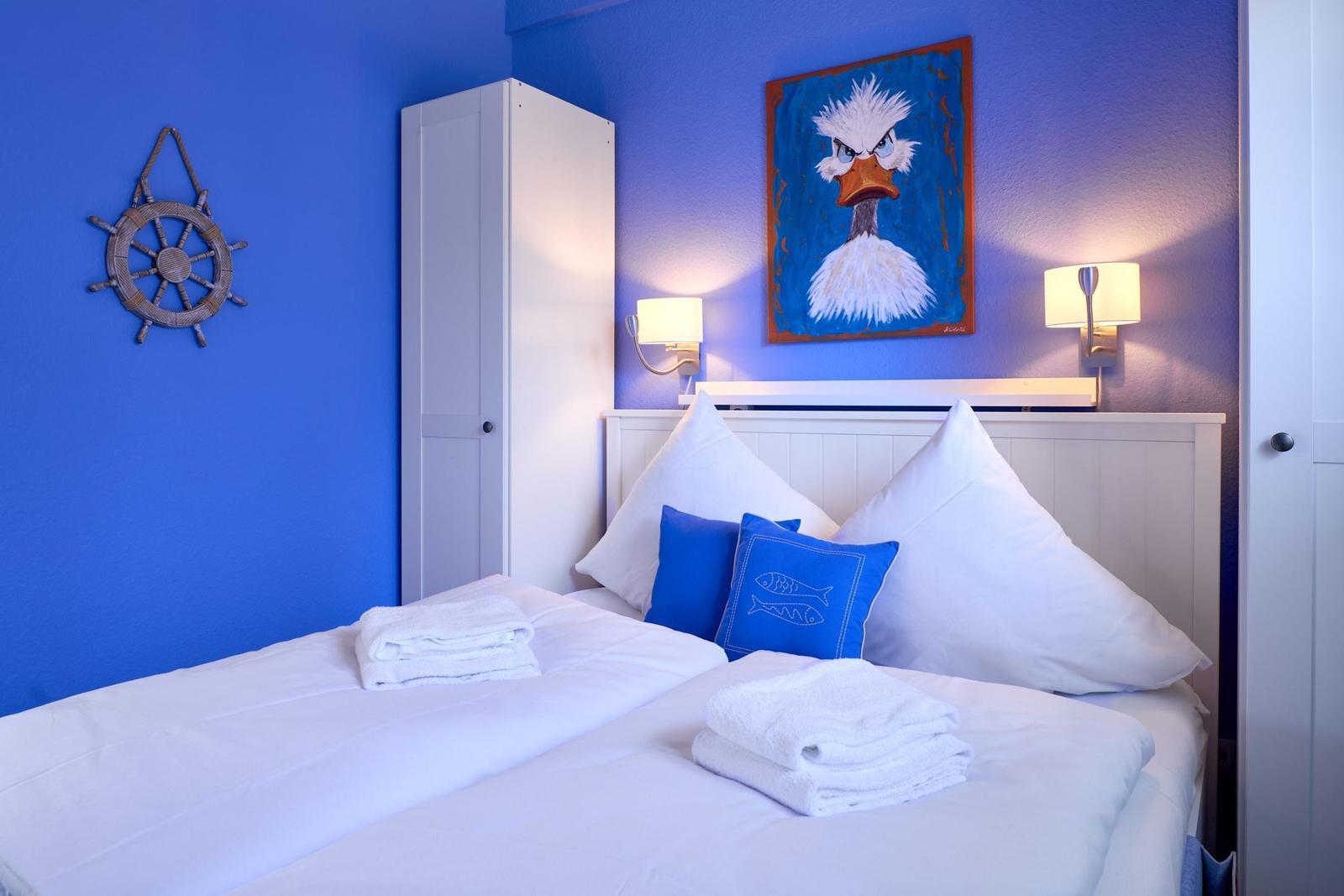 Schlafzimmer mit blauen Wänden, Bett mit Kissen und Wandbild eines Vogels.