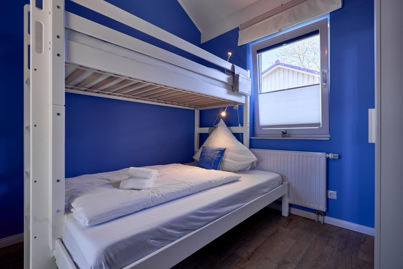 Zimmer mit Doppelstockbett, blauen Wänden und Fenster mit Blick nach draußen.