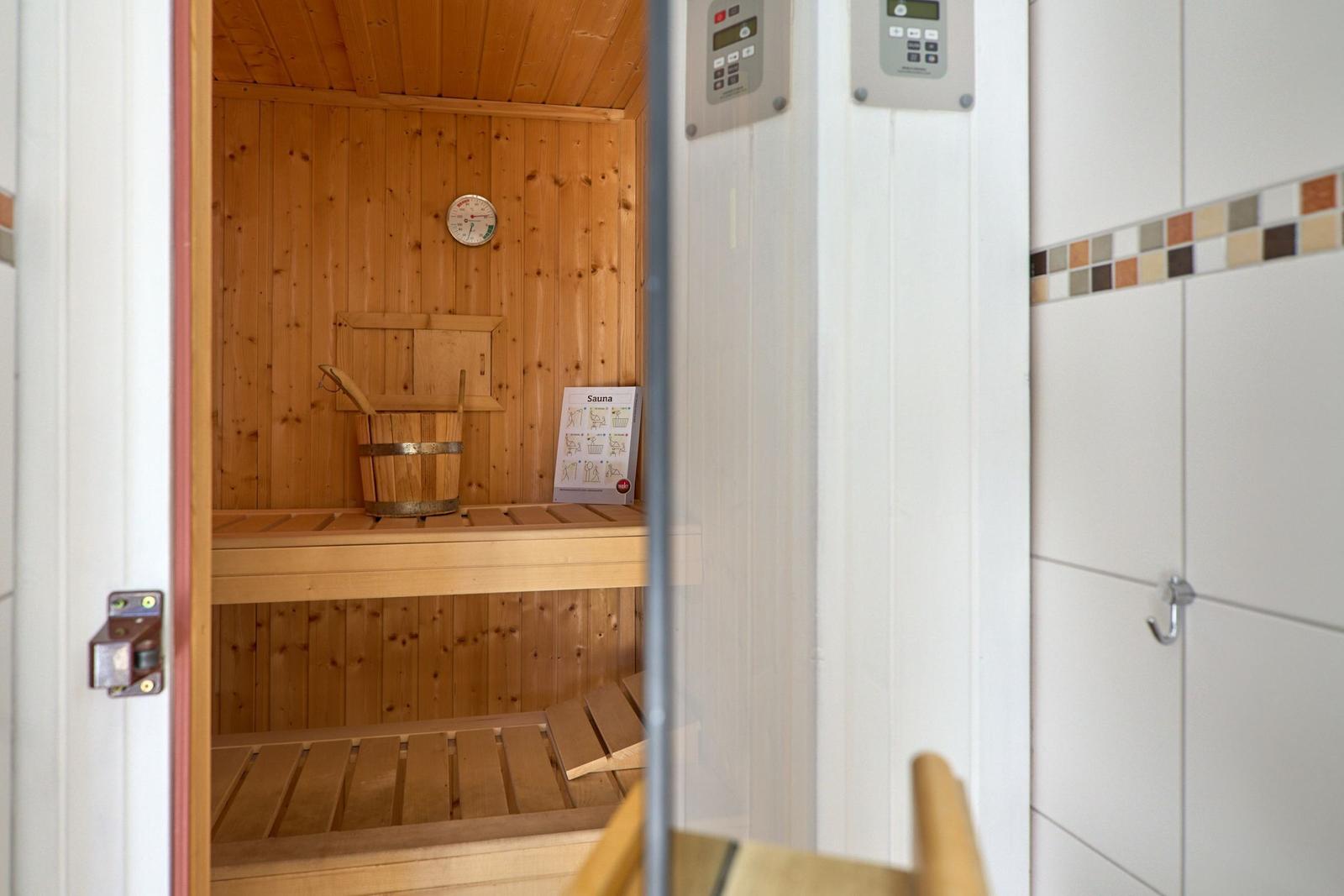 Sauna mit Holzwand, Sitzbänken und Thermometer. Steuerung an der Tür.