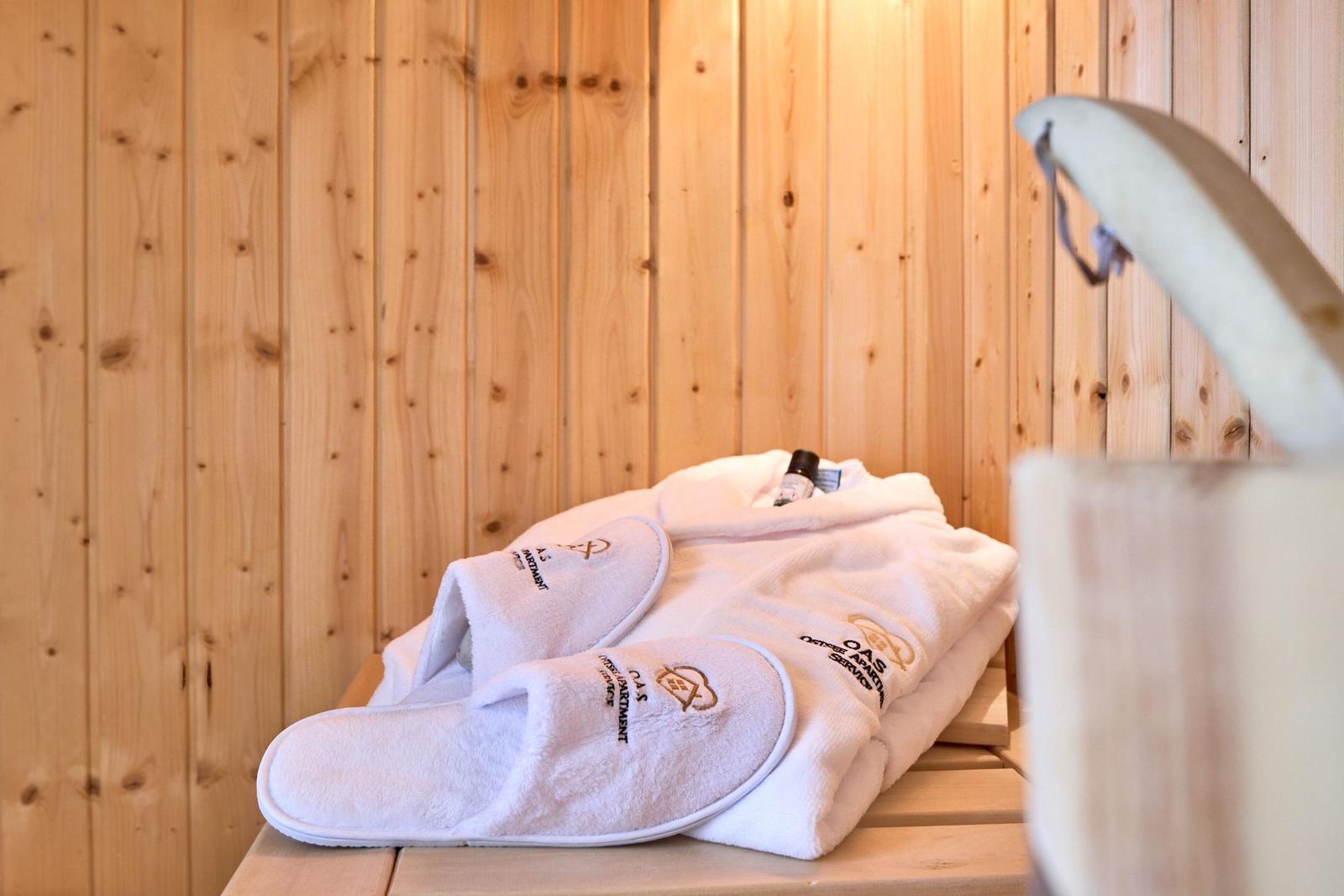 Weißer Bademantel und Hausschuhe liegen auf einer Holzbank in einer Sauna.