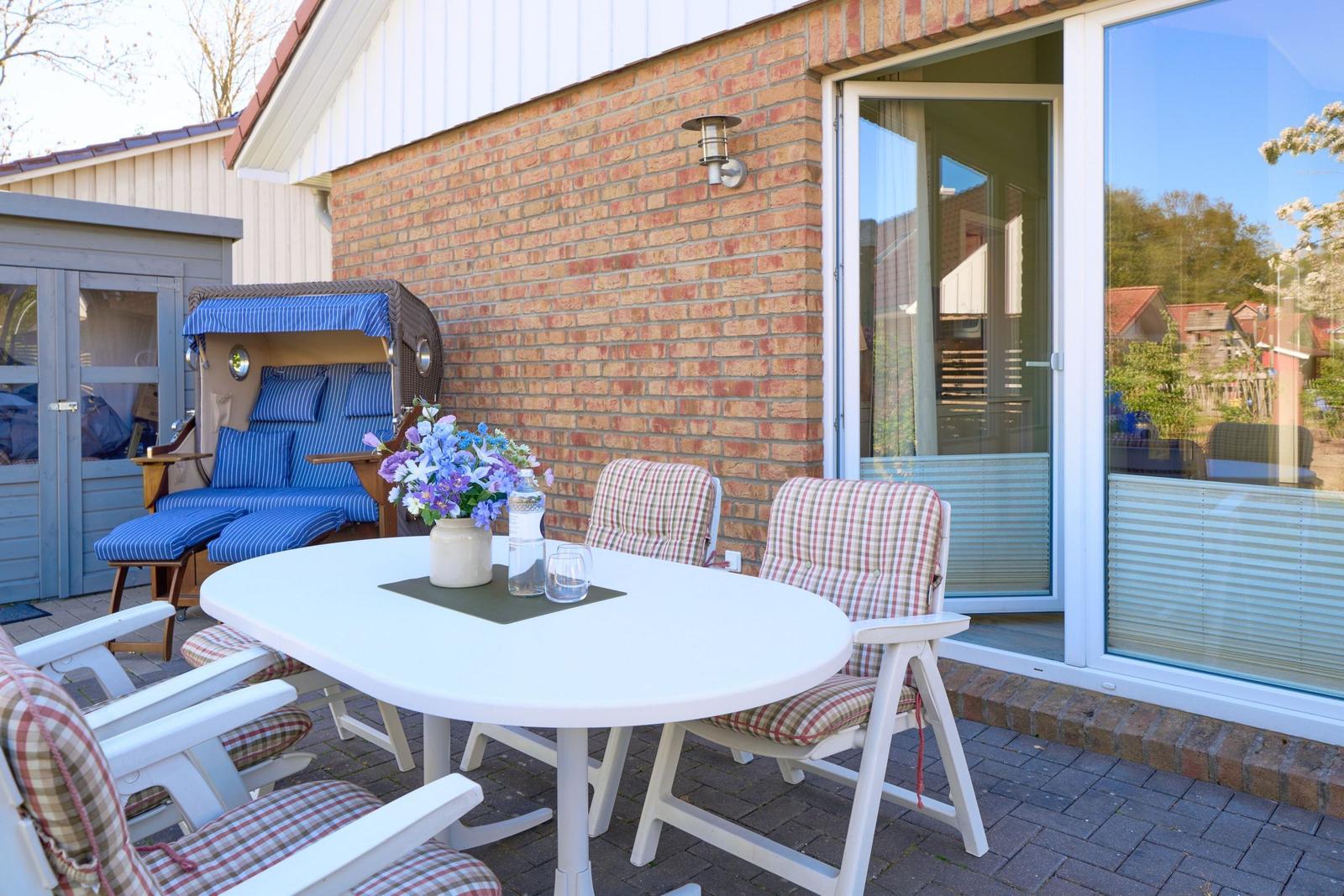 Terrasse mit weißem Tisch, Stühlen und Liegestuhl vor Backsteinhaus