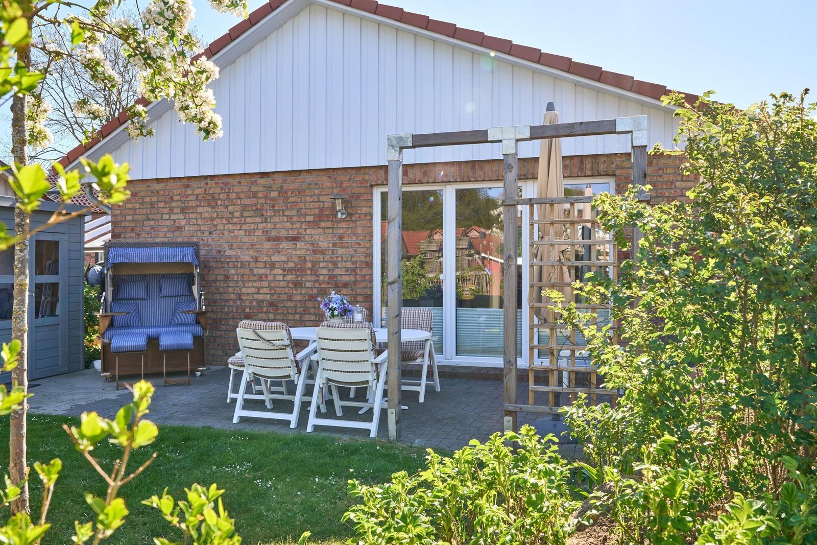 Terrasse mit Tisch, Stühlen und Sonnenschutz neben Haus mit Ziegelwand und weißen Holzverkleidungen.