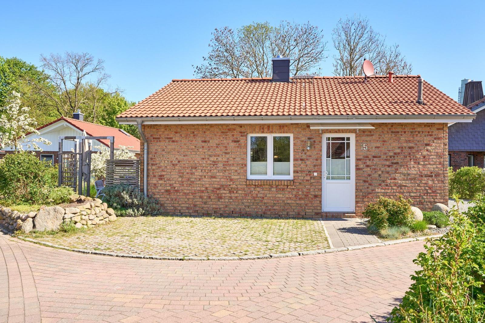 Einzelne Villa mit rotem Dach und Backsteinfassade. Vorgarten mit Steinmauer und gepflastertem Weg.