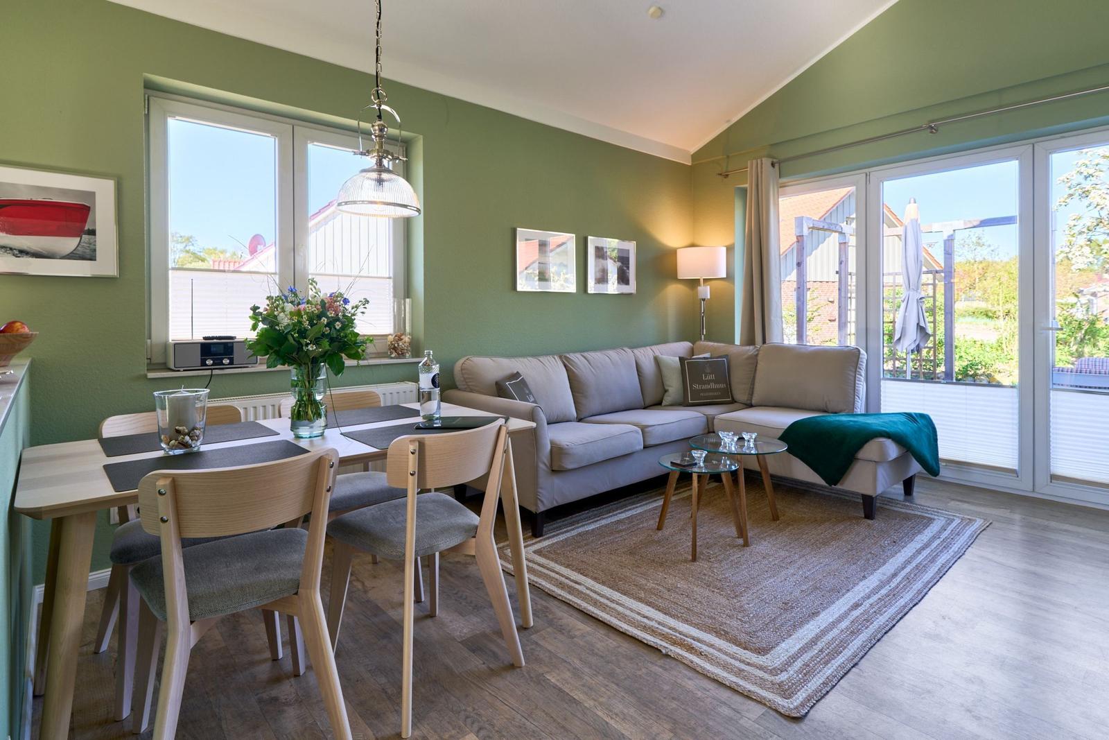 Wohn- und Essbereich mit Sofa, Tisch und Stühlen. Grüne Wände und große Fenster.