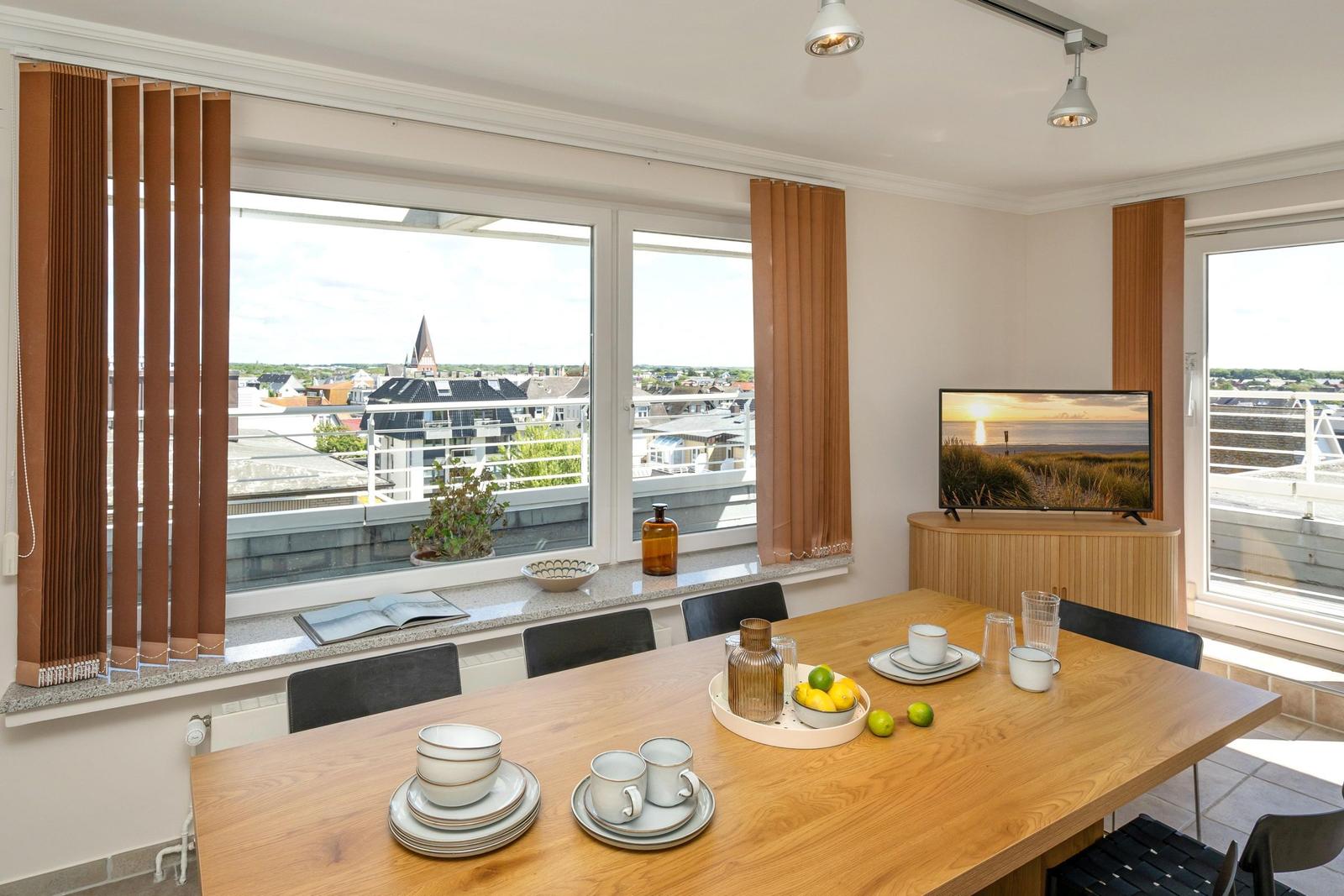Essbereich mit Tisch, Stühlen und Blick auf Dächer. Fernseher auf Holzschrank.
