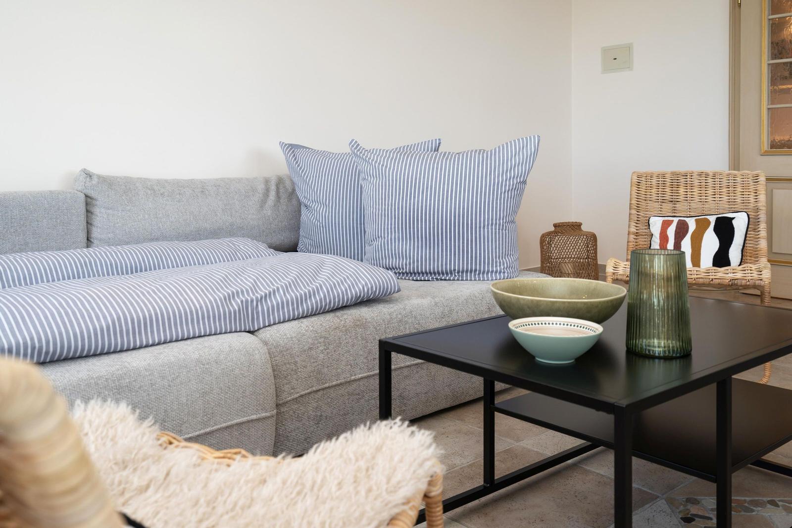 Ein Wohnzimmer mit grauem Sofa, gestreiften Kissen und einem schwarzen Couchtisch.