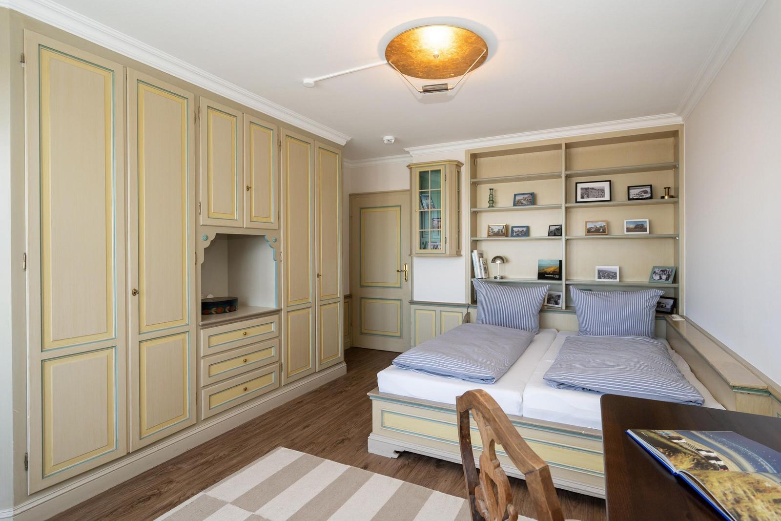 Schlafzimmer mit Doppelbett, Schrank und Bücherregal. Holzboden und Deckenleuchte.