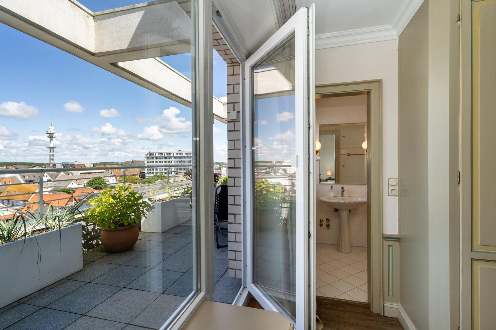 Terrasse mit Blick auf Stadt und Turm. Hinter dem Fenster Badezimmer mit Waschbecken.