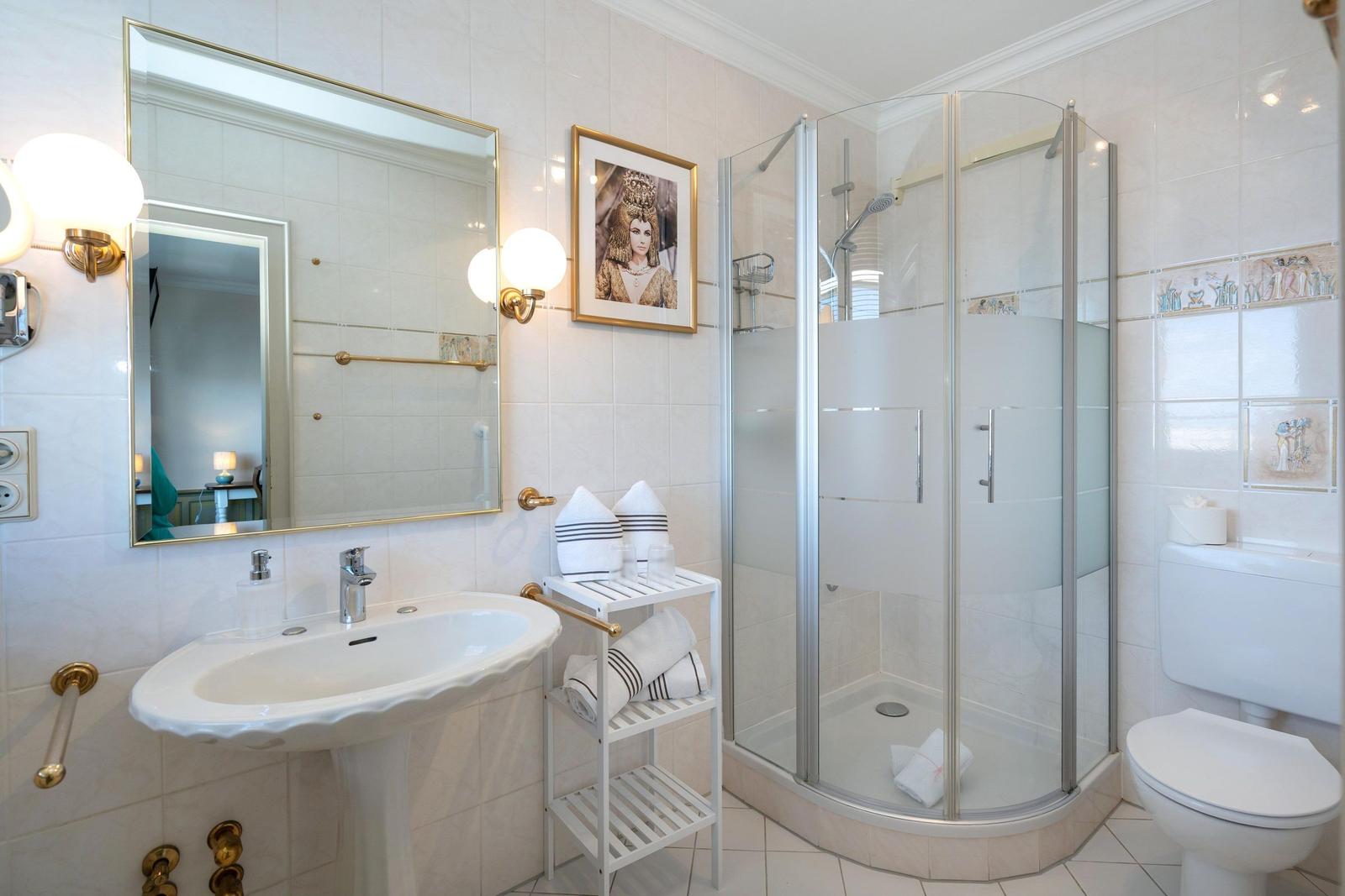 Badezimmer mit Dusche, Waschbecken und Toilette. Fliesenwand und Spiegel mit goldener Fassung.