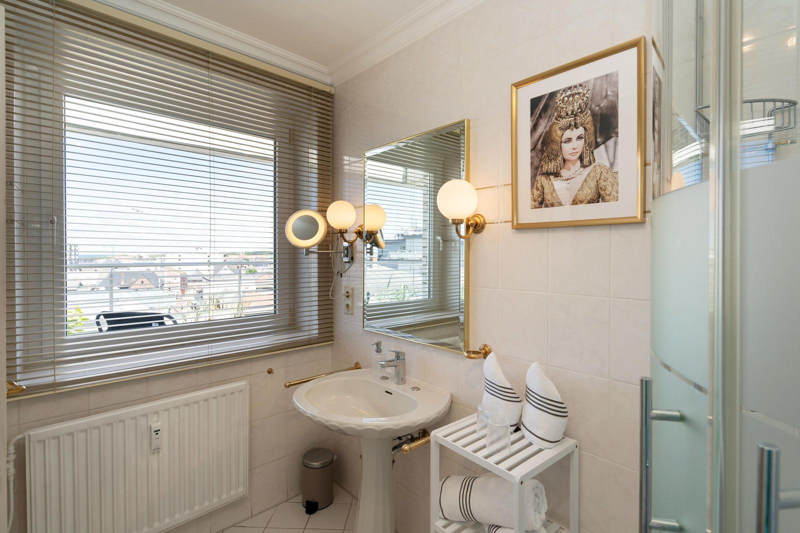 Badezimmer mit Waschbecken, Spiegel, Dusche und Fenster mit Blick.