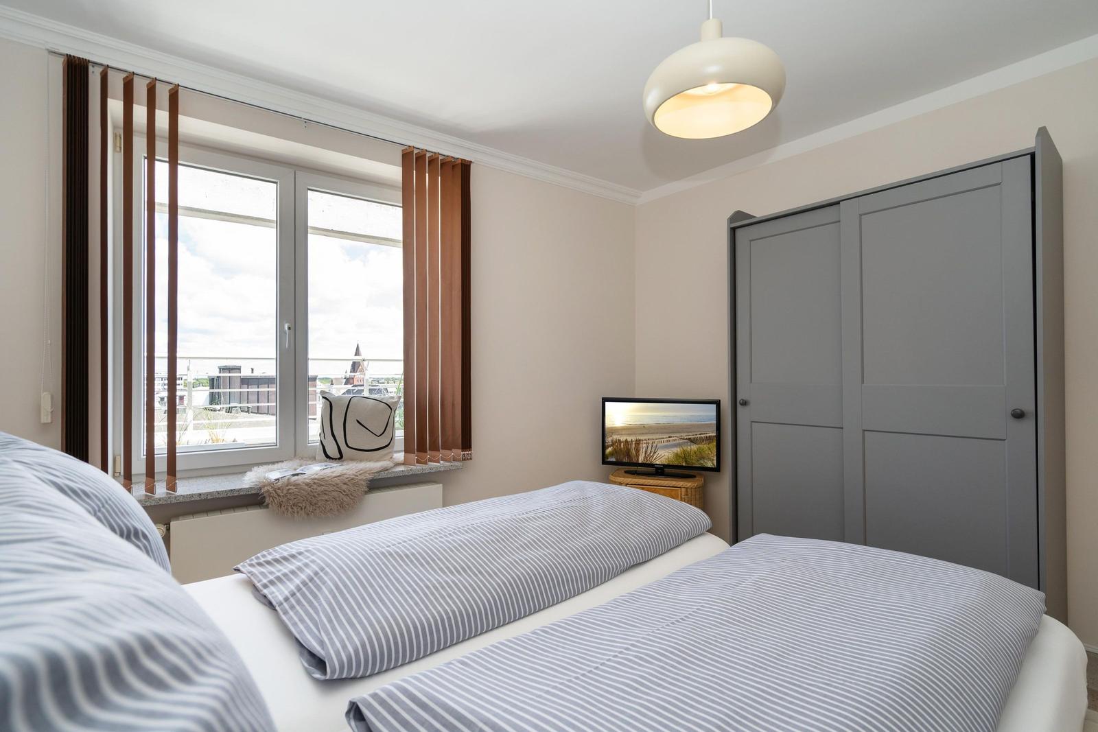 Schlafzimmer mit Doppelbett, Fenster und Kleiderschrank.
