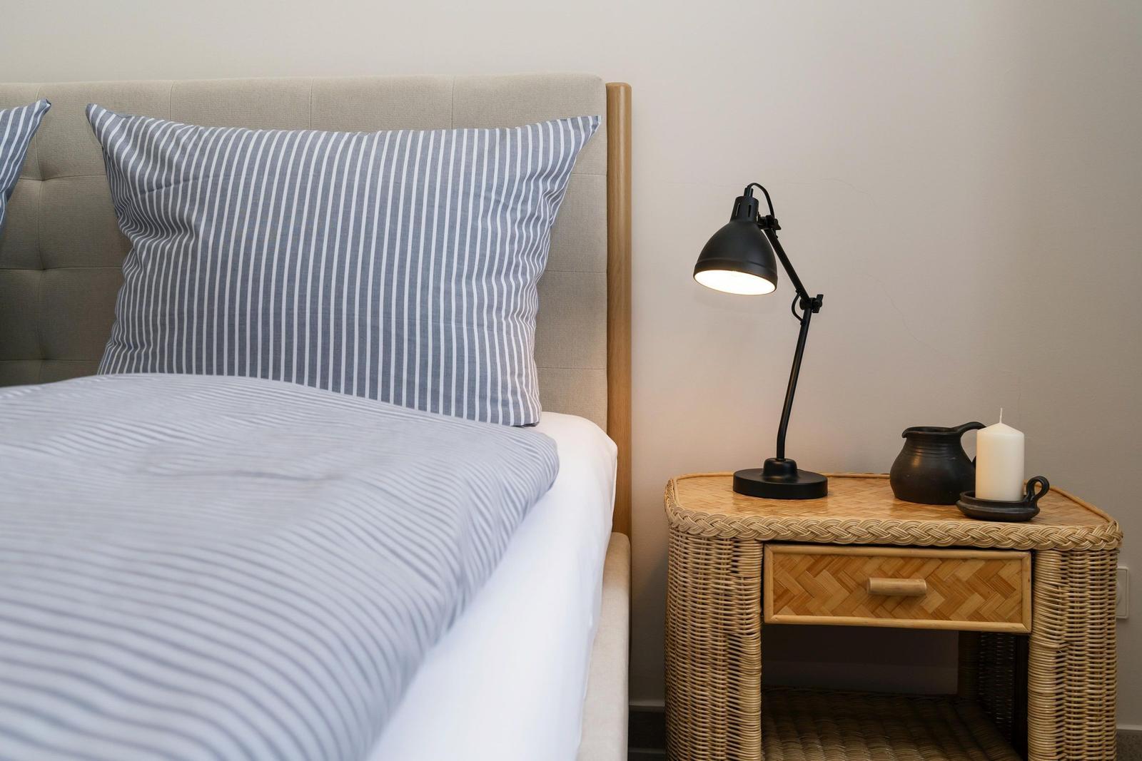 Schlafzimmer mit Bett, Kissen und Nachttisch mit Lampe und Kerze.