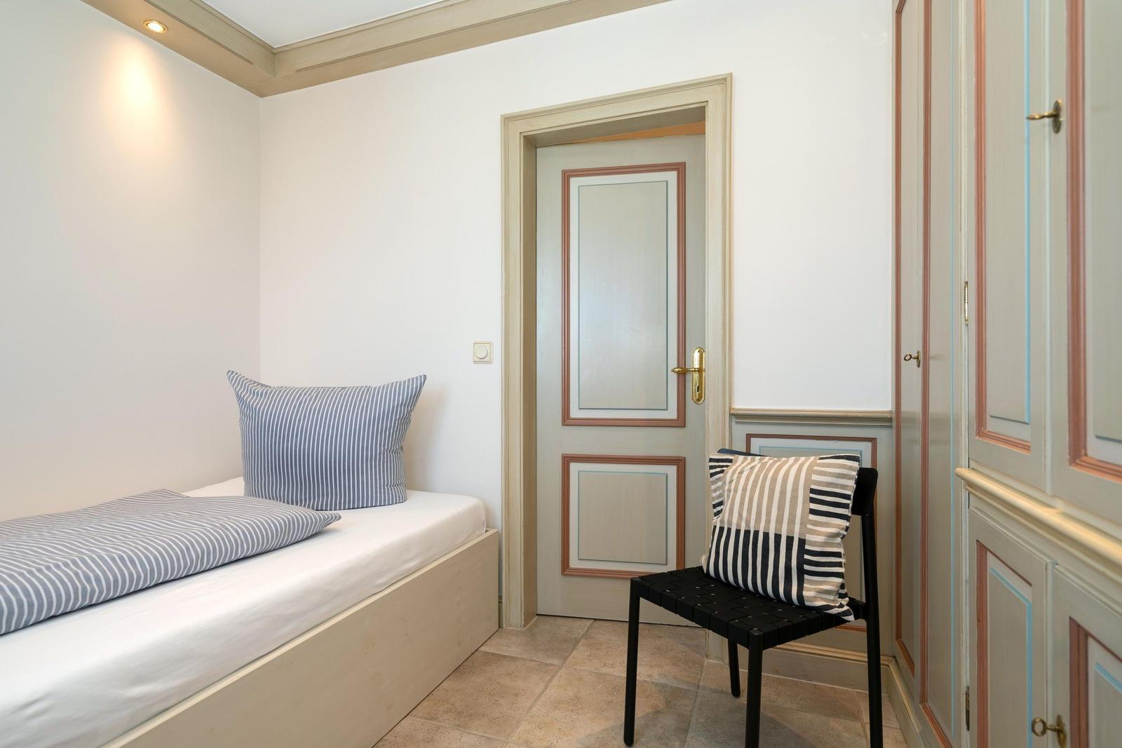 Schlafzimmer mit Bett, Stuhl und Kleiderschrank. Tür und Wände mit Holzrahmen.
