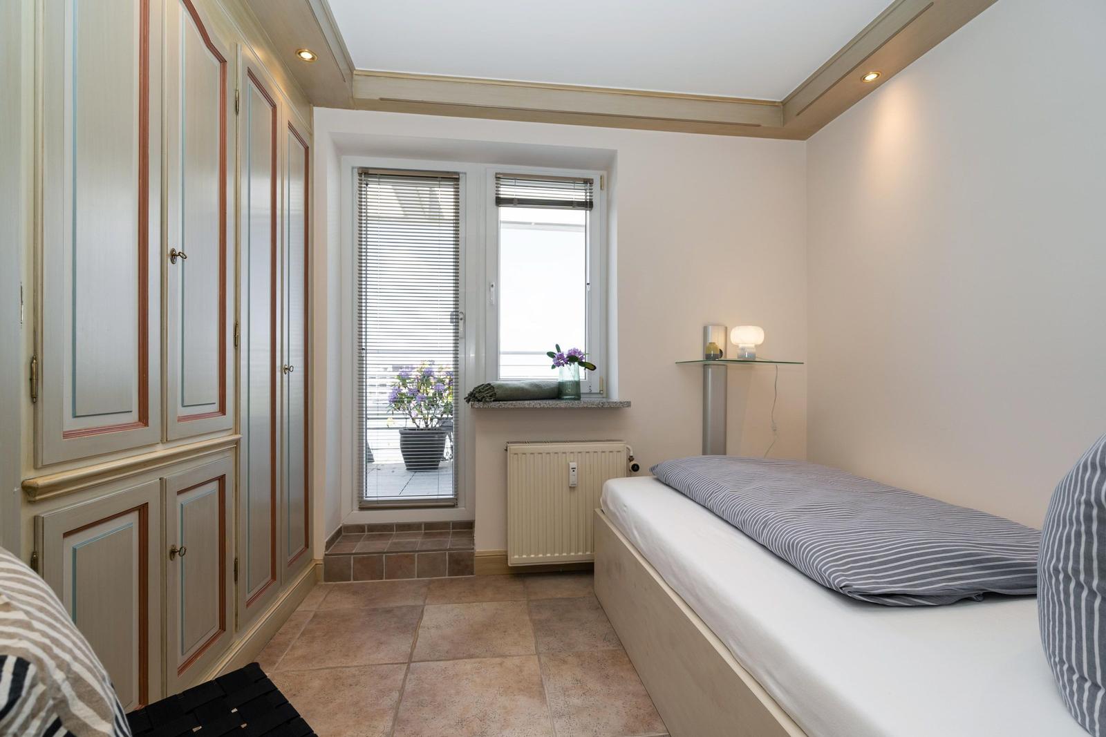 Schlafzimmer mit Bett, Kleiderschrank und Fenster mit Blumen.