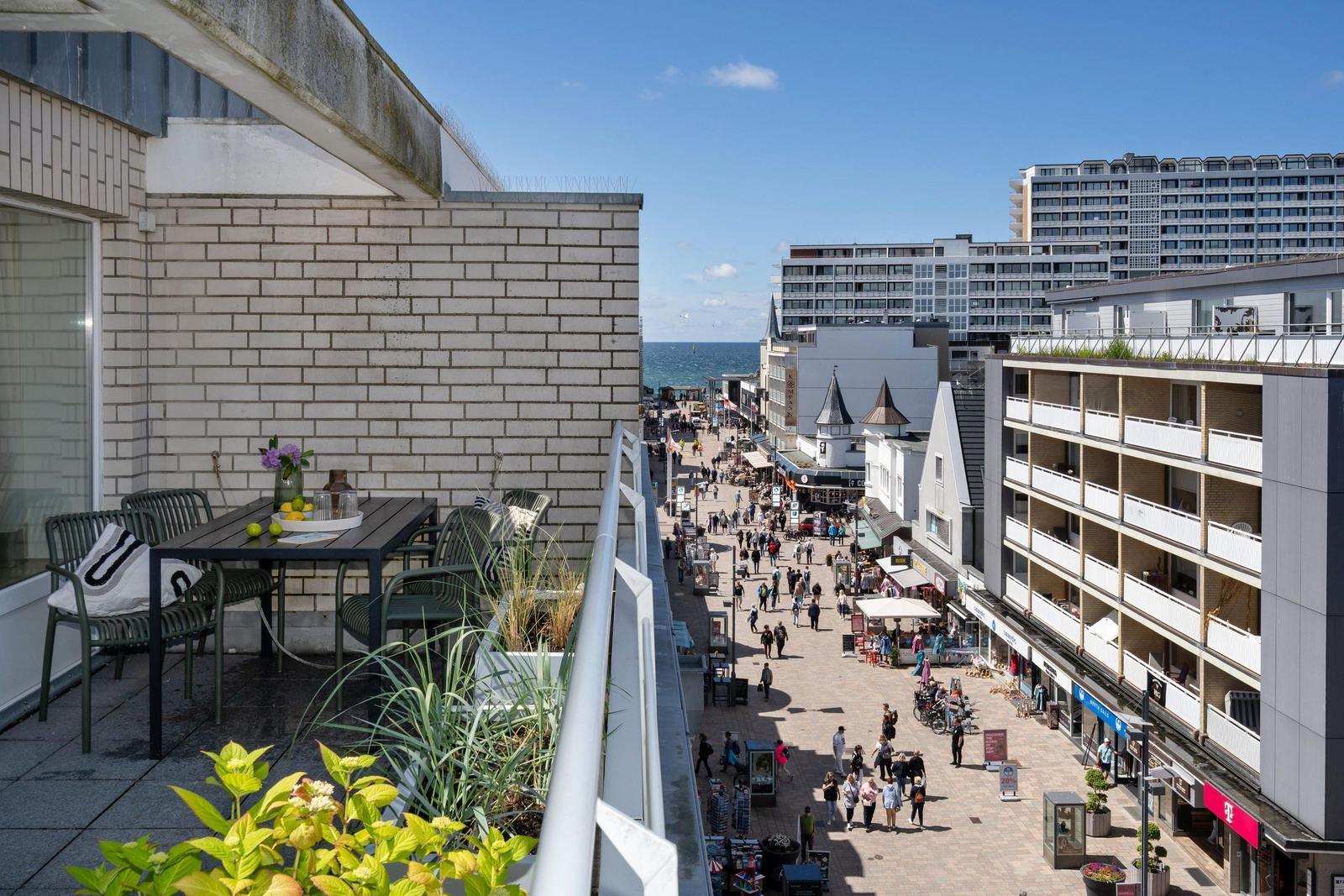 Terrasse mit Tisch und Stühlen, Blick auf belebte Straße und Meer.