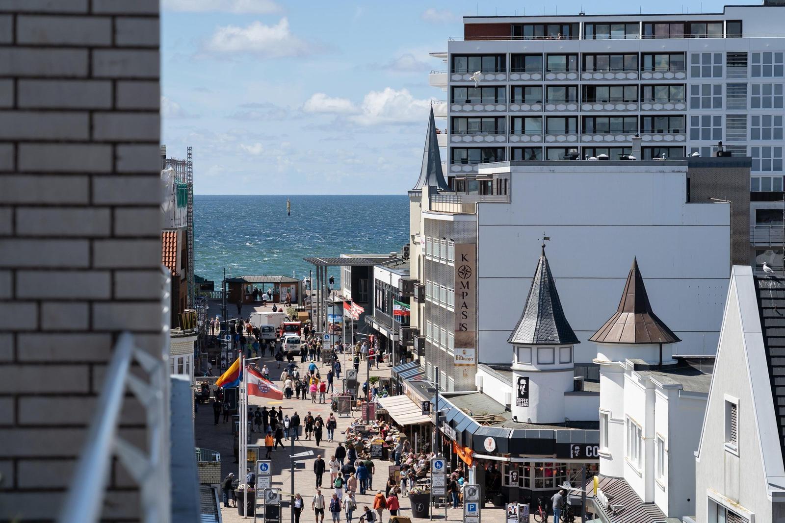 Stadtansicht mit Strand, Geschäften und Hochhäusern. Menschen gehen auf dem belebten Platz.